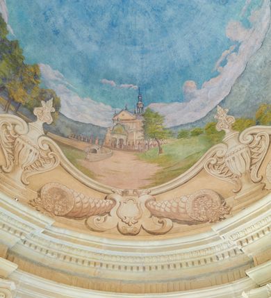 Zdjęcie nr 2: Polichromia umieszczona na półeliptycznej kopule nad kruchtą północną. Przedstawienie ujęte dekoracyjną ramą o fantazyjnym wykroju zdobioną klasycystycznymi wazonami, kartuszami i rogami obfitości. W dolnej części na jasnoczerwonej chmurze ukazane przedstawienie Zaśnięcia Najświętszej Marii Panny. Matka Boska wyobrażona w pozycji leżącej na prześcieradle unoszonym przez grupę aniołów. Maria leży z głową z lewej strony kompozycji z rękami złożonymi na piersi i z ugiętymi w kolanach nogami. Jest ubrana w jasnoróżową suknię, biały welon na głowie oraz niebieski płaszcz ułożony na jej nogach. Aniołowie są ubrani w różnokolorowe tuniki i płaszcze, mają też różne kolory skrzydeł. Przedstawienie okalają uskrzydlone główki aniołków oraz trójka półnagich putt sypiących kwiatki. W górnej części polichromii znajduje się odwrócony pejzaż z przedstawieniem kościoła w Brodach. W centrum jasnobłękitne niebo, a dookoła zielony pejzaż z drzewami. 