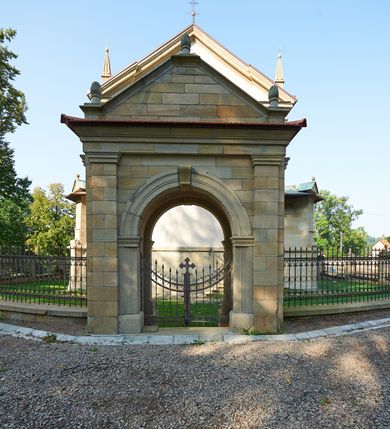 Zdjęcie nr 62: Kościół należy do zespołu dróżek Matki Boskiej, położnych w obrębie klasztoru w Kalwarii Zebrzydowskiej. Świątynia jest położna w centrum wsi, na wschód od głównej drogi, na placu otoczonym kamiennym murem z żeliwnym płotem, który od frontu ozdobiony jest figurami 12 apostołów, umieszczonymi na wysokich cokołach. Główne wejście na plac prowadzi przez bramę od zachodu, flankowaną dwoma filarami, na których ustawione są klasycystyczne wazony. Drugie wejście usytuowane jest od wschodu przez murowaną bramę, nakrytą daszkiem dwuspadowym, na którym ustawiona jest figura grającego na trąbie anioła. Trzecie wejście znajduje się od północy.

Kościół jest budowlą orientowaną, założoną na planie prostokąta, jednonawową, zamkniętą półkolistą absydą. Od zachodu przylega kruchta na planie prostokąta, zamkniętego z jednej strony półkoliście. Wewnątrz kościół dwupiętrowy. Na parterze część wschodnia świątyni podniesiona jest o siedem stopni, oddzielona od nawy trzema półkolistymi arkadami, wspartymi na czterech filarach i ustawionymi przed nimi półkolumnami, które wspierają pełne belkowanie, wyłamane na osiach. W przyłuczach płskorzeźbione główki aniołków. Na fryzie złocony napis: „EIA ADVOCATA NOSTRA OCVLOS MISERICORDES AD NOS CONVERTE ET IESVM BENEDICTV FRCTVM NOBIS OSTENDE”. Za środkową arkadą usytuowana jest niewielka, najstarsza część świątyni – Grób Matki Boskiej, na rzucie prostokąta, sklepiony krzyżowo. W ścianach bocznych nawy są półkoliście zamknięte wnęki na ołtarze. Od zachodu chór muzyczny wsparty jest na trzech arkadach filarowych. Wnętrze obiega drewniany ganek wsparty na metalowych wspornikach, a w części wschodniej i zachodniej na trzech murowanych arkadach. Podniebienie ganku zdobione jest geometrycznym stiukiem. W części nawowej świątyni znajduje się sklepienie kolebkowe z lunetami, w apsydzie hemisferyczne. Wnętrze doświetlone jest sześcioma małymi, okrągłymi oknami znajdującymi się na piętrze od strony północnej i południowej.

Fasada w dolnej części zaakcentowana jest przez monumentalną kruchtę w formie aediculi, założoną na rzucie prostokąta zamkniętego półkoliście. Ściany artykułowane są pięcioma półkolistymi arkadami, wspartymi na filarkach. Od zewnątrz osie ujęte są przez kanelowane kolumny, ustawione na wysokich cokołach, na tle pilastrów. Podpory wznoszą pełne belkowanie i wysunięty gzyms zdobiony kimationem i dekoracją kostkową. Nakrycie w formie kopuły półkolistej z latarnią. Belkowanie ozdobione jest dekoracją roślinną i główkami aniołków. Po bokach kruchty wysunięte są fragmenty muru oporowego do połowy wysokości fasady. Powyżej fasada flankowana przez dwie pary pilastrów z jońskimi kapitelami wspierającymi niepełne belkowanie. Pośrodku duże, półkoliste okno z metalową, dekoracyjną kratą. Szczyt trójkątny z oculusem pośrodku. Na szczycie ustawiona jest figura Najświętszej Marii Panny. Świątynia dookoła obwiedziona szerokim murem oporowym, nakrytym daszkiem, o ukośnych ścianach, flankowanych szkarpami, po sześć na każdej ścianie bocznej i dwoma na ścianie zachodniej oraz wschodniej. Powyżej elewacje ujęte pilastrami z kapitelami jońskimi wznoszącymi niepełne belkowanie. Na wschodniej ścianie półkolista apsyda, nakryta półkopułą. Kościół nakryty dachem siodłowym ze zdwojoną, wysoką latarnią pośrodku. Na narożach dachu ustawione wysokie obeliski na cokołach. 

 