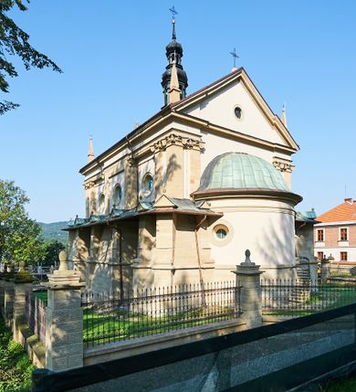 Zdjęcie nr 13: Kościół należy do zespołu dróżek Matki Boskiej, położnych w obrębie klasztoru w Kalwarii Zebrzydowskiej. Świątynia jest położna w centrum wsi, na wschód od głównej drogi, na placu otoczonym kamiennym murem z żeliwnym płotem, który od frontu ozdobiony jest figurami 12 apostołów, umieszczonymi na wysokich cokołach. Główne wejście na plac prowadzi przez bramę od zachodu, flankowaną dwoma filarami, na których ustawione są klasycystyczne wazony. Drugie wejście usytuowane jest od wschodu przez murowaną bramę, nakrytą daszkiem dwuspadowym, na którym ustawiona jest figura grającego na trąbie anioła. Trzecie wejście znajduje się od północy.

Kościół jest budowlą orientowaną, założoną na planie prostokąta, jednonawową, zamkniętą półkolistą absydą. Od zachodu przylega kruchta na planie prostokąta, zamkniętego z jednej strony półkoliście. Wewnątrz kościół dwupiętrowy. Na parterze część wschodnia świątyni podniesiona jest o siedem stopni, oddzielona od nawy trzema półkolistymi arkadami, wspartymi na czterech filarach i ustawionymi przed nimi półkolumnami, które wspierają pełne belkowanie, wyłamane na osiach. W przyłuczach płskorzeźbione główki aniołków. Na fryzie złocony napis: „EIA ADVOCATA NOSTRA OCVLOS MISERICORDES AD NOS CONVERTE ET IESVM BENEDICTV FRCTVM NOBIS OSTENDE”. Za środkową arkadą usytuowana jest niewielka, najstarsza część świątyni – Grób Matki Boskiej, na rzucie prostokąta, sklepiony krzyżowo. W ścianach bocznych nawy są półkoliście zamknięte wnęki na ołtarze. Od zachodu chór muzyczny wsparty jest na trzech arkadach filarowych. Wnętrze obiega drewniany ganek wsparty na metalowych wspornikach, a w części wschodniej i zachodniej na trzech murowanych arkadach. Podniebienie ganku zdobione jest geometrycznym stiukiem. W części nawowej świątyni znajduje się sklepienie kolebkowe z lunetami, w apsydzie hemisferyczne. Wnętrze doświetlone jest sześcioma małymi, okrągłymi oknami znajdującymi się na piętrze od strony północnej i południowej.

Fasada w dolnej części zaakcentowana jest przez monumentalną kruchtę w formie aediculi, założoną na rzucie prostokąta zamkniętego półkoliście. Ściany artykułowane są pięcioma półkolistymi arkadami, wspartymi na filarkach. Od zewnątrz osie ujęte są przez kanelowane kolumny, ustawione na wysokich cokołach, na tle pilastrów. Podpory wznoszą pełne belkowanie i wysunięty gzyms zdobiony kimationem i dekoracją kostkową. Nakrycie w formie kopuły półkolistej z latarnią. Belkowanie ozdobione jest dekoracją roślinną i główkami aniołków. Po bokach kruchty wysunięte są fragmenty muru oporowego do połowy wysokości fasady. Powyżej fasada flankowana przez dwie pary pilastrów z jońskimi kapitelami wspierającymi niepełne belkowanie. Pośrodku duże, półkoliste okno z metalową, dekoracyjną kratą. Szczyt trójkątny z oculusem pośrodku. Na szczycie ustawiona jest figura Najświętszej Marii Panny. Świątynia dookoła obwiedziona szerokim murem oporowym, nakrytym daszkiem, o ukośnych ścianach, flankowanych szkarpami, po sześć na każdej ścianie bocznej i dwoma na ścianie zachodniej oraz wschodniej. Powyżej elewacje ujęte pilastrami z kapitelami jońskimi wznoszącymi niepełne belkowanie. Na wschodniej ścianie półkolista apsyda, nakryta półkopułą. Kościół nakryty dachem siodłowym ze zdwojoną, wysoką latarnią pośrodku. Na narożach dachu ustawione wysokie obeliski na cokołach. 

 