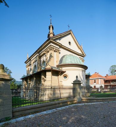 Zdjęcie nr 1: Kościół należy do zespołu dróżek Matki Boskiej, położnych w obrębie klasztoru w Kalwarii Zebrzydowskiej. Świątynia jest położna w centrum wsi, na wschód od głównej drogi, na placu otoczonym kamiennym murem z żeliwnym płotem, który od frontu ozdobiony jest figurami 12 apostołów, umieszczonymi na wysokich cokołach. Główne wejście na plac prowadzi przez bramę od zachodu, flankowaną dwoma filarami, na których ustawione są klasycystyczne wazony. Drugie wejście usytuowane jest od wschodu przez murowaną bramę, nakrytą daszkiem dwuspadowym, na którym ustawiona jest figura grającego na trąbie anioła. Trzecie wejście znajduje się od północy.

Kościół jest budowlą orientowaną, założoną na planie prostokąta, jednonawową, zamkniętą półkolistą absydą. Od zachodu przylega kruchta na planie prostokąta, zamkniętego z jednej strony półkoliście. Wewnątrz kościół dwupiętrowy. Na parterze część wschodnia świątyni podniesiona jest o siedem stopni, oddzielona od nawy trzema półkolistymi arkadami, wspartymi na czterech filarach i ustawionymi przed nimi półkolumnami, które wspierają pełne belkowanie, wyłamane na osiach. W przyłuczach płskorzeźbione główki aniołków. Na fryzie złocony napis: „EIA ADVOCATA NOSTRA OCVLOS MISERICORDES AD NOS CONVERTE ET IESVM BENEDICTV FRCTVM NOBIS OSTENDE”. Za środkową arkadą usytuowana jest niewielka, najstarsza część świątyni – Grób Matki Boskiej, na rzucie prostokąta, sklepiony krzyżowo. W ścianach bocznych nawy są półkoliście zamknięte wnęki na ołtarze. Od zachodu chór muzyczny wsparty jest na trzech arkadach filarowych. Wnętrze obiega drewniany ganek wsparty na metalowych wspornikach, a w części wschodniej i zachodniej na trzech murowanych arkadach. Podniebienie ganku zdobione jest geometrycznym stiukiem. W części nawowej świątyni znajduje się sklepienie kolebkowe z lunetami, w apsydzie hemisferyczne. Wnętrze doświetlone jest sześcioma małymi, okrągłymi oknami znajdującymi się na piętrze od strony północnej i południowej.

Fasada w dolnej części zaakcentowana jest przez monumentalną kruchtę w formie aediculi, założoną na rzucie prostokąta zamkniętego półkoliście. Ściany artykułowane są pięcioma półkolistymi arkadami, wspartymi na filarkach. Od zewnątrz osie ujęte są przez kanelowane kolumny, ustawione na wysokich cokołach, na tle pilastrów. Podpory wznoszą pełne belkowanie i wysunięty gzyms zdobiony kimationem i dekoracją kostkową. Nakrycie w formie kopuły półkolistej z latarnią. Belkowanie ozdobione jest dekoracją roślinną i główkami aniołków. Po bokach kruchty wysunięte są fragmenty muru oporowego do połowy wysokości fasady. Powyżej fasada flankowana przez dwie pary pilastrów z jońskimi kapitelami wspierającymi niepełne belkowanie. Pośrodku duże, półkoliste okno z metalową, dekoracyjną kratą. Szczyt trójkątny z oculusem pośrodku. Na szczycie ustawiona jest figura Najświętszej Marii Panny. Świątynia dookoła obwiedziona szerokim murem oporowym, nakrytym daszkiem, o ukośnych ścianach, flankowanych szkarpami, po sześć na każdej ścianie bocznej i dwoma na ścianie zachodniej oraz wschodniej. Powyżej elewacje ujęte pilastrami z kapitelami jońskimi wznoszącymi niepełne belkowanie. Na wschodniej ścianie półkolista apsyda, nakryta półkopułą. Kościół nakryty dachem siodłowym ze zdwojoną, wysoką latarnią pośrodku. Na narożach dachu ustawione wysokie obeliski na cokołach. 

 