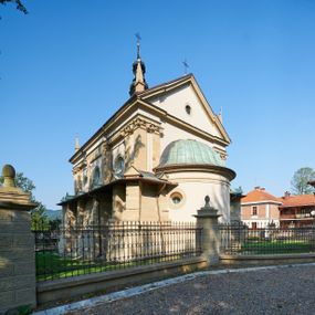 Zdjęcie nr 1: Kościół należy do zespołu dróżek Matki Boskiej, położnych w obrębie klasztoru w Kalwarii Zebrzydowskiej. Świątynia jest położna w centrum wsi, na wschód od głównej drogi, na placu otoczonym kamiennym murem z żeliwnym płotem, który od frontu ozdobiony jest figurami 12 apostołów, umieszczonymi na wysokich cokołach. Główne wejście na plac prowadzi przez bramę od zachodu, flankowaną dwoma filarami, na których ustawione są klasycystyczne wazony. Drugie wejście usytuowane jest od wschodu przez murowaną bramę, nakrytą daszkiem dwuspadowym, na którym ustawiona jest figura grającego na trąbie anioła. Trzecie wejście znajduje się od północy.

Kościół jest budowlą orientowaną, założoną na planie prostokąta, jednonawową, zamkniętą półkolistą absydą. Od zachodu przylega kruchta na planie prostokąta, zamkniętego z jednej strony półkoliście. Wewnątrz kościół dwupiętrowy. Na parterze część wschodnia świątyni podniesiona jest o siedem stopni, oddzielona od nawy trzema półkolistymi arkadami, wspartymi na czterech filarach i ustawionymi przed nimi półkolumnami, które wspierają pełne belkowanie, wyłamane na osiach. W przyłuczach płskorzeźbione główki aniołków. Na fryzie złocony napis: „EIA ADVOCATA NOSTRA OCVLOS MISERICORDES AD NOS CONVERTE ET IESVM BENEDICTV FRCTVM NOBIS OSTENDE”. Za środkową arkadą usytuowana jest niewielka, najstarsza część świątyni – Grób Matki Boskiej, na rzucie prostokąta, sklepiony krzyżowo. W ścianach bocznych nawy są półkoliście zamknięte wnęki na ołtarze. Od zachodu chór muzyczny wsparty jest na trzech arkadach filarowych. Wnętrze obiega drewniany ganek wsparty na metalowych wspornikach, a w części wschodniej i zachodniej na trzech murowanych arkadach. Podniebienie ganku zdobione jest geometrycznym stiukiem. W części nawowej świątyni znajduje się sklepienie kolebkowe z lunetami, w apsydzie hemisferyczne. Wnętrze doświetlone jest sześcioma małymi, okrągłymi oknami znajdującymi się na piętrze od strony północnej i południowej.

Fasada w dolnej części zaakcentowana jest przez monumentalną kruchtę w formie aediculi, założoną na rzucie prostokąta zamkniętego półkoliście. Ściany artykułowane są pięcioma półkolistymi arkadami, wspartymi na filarkach. Od zewnątrz osie ujęte są przez kanelowane kolumny, ustawione na wysokich cokołach, na tle pilastrów. Podpory wznoszą pełne belkowanie i wysunięty gzyms zdobiony kimationem i dekoracją kostkową. Nakrycie w formie kopuły półkolistej z latarnią. Belkowanie ozdobione jest dekoracją roślinną i główkami aniołków. Po bokach kruchty wysunięte są fragmenty muru oporowego do połowy wysokości fasady. Powyżej fasada flankowana przez dwie pary pilastrów z jońskimi kapitelami wspierającymi niepełne belkowanie. Pośrodku duże, półkoliste okno z metalową, dekoracyjną kratą. Szczyt trójkątny z oculusem pośrodku. Na szczycie ustawiona jest figura Najświętszej Marii Panny. Świątynia dookoła obwiedziona szerokim murem oporowym, nakrytym daszkiem, o ukośnych ścianach, flankowanych szkarpami, po sześć na każdej ścianie bocznej i dwoma na ścianie zachodniej oraz wschodniej. Powyżej elewacje ujęte pilastrami z kapitelami jońskimi wznoszącymi niepełne belkowanie. Na wschodniej ścianie półkolista apsyda, nakryta półkopułą. Kościół nakryty dachem siodłowym ze zdwojoną, wysoką latarnią pośrodku. Na narożach dachu ustawione wysokie obeliski na cokołach. 

 