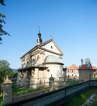 Zdjęcie nr 2: Kościół należy do zespołu dróżek Matki Boskiej, położnych w obrębie klasztoru w Kalwarii Zebrzydowskiej. Świątynia jest położna w centrum wsi, na wschód od głównej drogi, na placu otoczonym kamiennym murem z żeliwnym płotem, który od frontu ozdobiony jest figurami 12 apostołów, umieszczonymi na wysokich cokołach. Główne wejście na plac prowadzi przez bramę od zachodu, flankowaną dwoma filarami, na których ustawione są klasycystyczne wazony. Drugie wejście usytuowane jest od wschodu przez murowaną bramę, nakrytą daszkiem dwuspadowym, na którym ustawiona jest figura grającego na trąbie anioła. Trzecie wejście znajduje się od północy.

Kościół jest budowlą orientowaną, założoną na planie prostokąta, jednonawową, zamkniętą półkolistą absydą. Od zachodu przylega kruchta na planie prostokąta, zamkniętego z jednej strony półkoliście. Wewnątrz kościół dwupiętrowy. Na parterze część wschodnia świątyni podniesiona jest o siedem stopni, oddzielona od nawy trzema półkolistymi arkadami, wspartymi na czterech filarach i ustawionymi przed nimi półkolumnami, które wspierają pełne belkowanie, wyłamane na osiach. W przyłuczach płskorzeźbione główki aniołków. Na fryzie złocony napis: „EIA ADVOCATA NOSTRA OCVLOS MISERICORDES AD NOS CONVERTE ET IESVM BENEDICTV FRCTVM NOBIS OSTENDE”. Za środkową arkadą usytuowana jest niewielka, najstarsza część świątyni – Grób Matki Boskiej, na rzucie prostokąta, sklepiony krzyżowo. W ścianach bocznych nawy są półkoliście zamknięte wnęki na ołtarze. Od zachodu chór muzyczny wsparty jest na trzech arkadach filarowych. Wnętrze obiega drewniany ganek wsparty na metalowych wspornikach, a w części wschodniej i zachodniej na trzech murowanych arkadach. Podniebienie ganku zdobione jest geometrycznym stiukiem. W części nawowej świątyni znajduje się sklepienie kolebkowe z lunetami, w apsydzie hemisferyczne. Wnętrze doświetlone jest sześcioma małymi, okrągłymi oknami znajdującymi się na piętrze od strony północnej i południowej.

Fasada w dolnej części zaakcentowana jest przez monumentalną kruchtę w formie aediculi, założoną na rzucie prostokąta zamkniętego półkoliście. Ściany artykułowane są pięcioma półkolistymi arkadami, wspartymi na filarkach. Od zewnątrz osie ujęte są przez kanelowane kolumny, ustawione na wysokich cokołach, na tle pilastrów. Podpory wznoszą pełne belkowanie i wysunięty gzyms zdobiony kimationem i dekoracją kostkową. Nakrycie w formie kopuły półkolistej z latarnią. Belkowanie ozdobione jest dekoracją roślinną i główkami aniołków. Po bokach kruchty wysunięte są fragmenty muru oporowego do połowy wysokości fasady. Powyżej fasada flankowana przez dwie pary pilastrów z jońskimi kapitelami wspierającymi niepełne belkowanie. Pośrodku duże, półkoliste okno z metalową, dekoracyjną kratą. Szczyt trójkątny z oculusem pośrodku. Na szczycie ustawiona jest figura Najświętszej Marii Panny. Świątynia dookoła obwiedziona szerokim murem oporowym, nakrytym daszkiem, o ukośnych ścianach, flankowanych szkarpami, po sześć na każdej ścianie bocznej i dwoma na ścianie zachodniej oraz wschodniej. Powyżej elewacje ujęte pilastrami z kapitelami jońskimi wznoszącymi niepełne belkowanie. Na wschodniej ścianie półkolista apsyda, nakryta półkopułą. Kościół nakryty dachem siodłowym ze zdwojoną, wysoką latarnią pośrodku. Na narożach dachu ustawione wysokie obeliski na cokołach. 

 