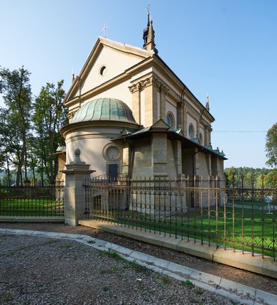 Zdjęcie nr 35: Kościół należy do zespołu dróżek Matki Boskiej, położnych w obrębie klasztoru w Kalwarii Zebrzydowskiej. Świątynia jest położna w centrum wsi, na wschód od głównej drogi, na placu otoczonym kamiennym murem z żeliwnym płotem, który od frontu ozdobiony jest figurami 12 apostołów, umieszczonymi na wysokich cokołach. Główne wejście na plac prowadzi przez bramę od zachodu, flankowaną dwoma filarami, na których ustawione są klasycystyczne wazony. Drugie wejście usytuowane jest od wschodu przez murowaną bramę, nakrytą daszkiem dwuspadowym, na którym ustawiona jest figura grającego na trąbie anioła. Trzecie wejście znajduje się od północy.

Kościół jest budowlą orientowaną, założoną na planie prostokąta, jednonawową, zamkniętą półkolistą absydą. Od zachodu przylega kruchta na planie prostokąta, zamkniętego z jednej strony półkoliście. Wewnątrz kościół dwupiętrowy. Na parterze część wschodnia świątyni podniesiona jest o siedem stopni, oddzielona od nawy trzema półkolistymi arkadami, wspartymi na czterech filarach i ustawionymi przed nimi półkolumnami, które wspierają pełne belkowanie, wyłamane na osiach. W przyłuczach płskorzeźbione główki aniołków. Na fryzie złocony napis: „EIA ADVOCATA NOSTRA OCVLOS MISERICORDES AD NOS CONVERTE ET IESVM BENEDICTV FRCTVM NOBIS OSTENDE”. Za środkową arkadą usytuowana jest niewielka, najstarsza część świątyni – Grób Matki Boskiej, na rzucie prostokąta, sklepiony krzyżowo. W ścianach bocznych nawy są półkoliście zamknięte wnęki na ołtarze. Od zachodu chór muzyczny wsparty jest na trzech arkadach filarowych. Wnętrze obiega drewniany ganek wsparty na metalowych wspornikach, a w części wschodniej i zachodniej na trzech murowanych arkadach. Podniebienie ganku zdobione jest geometrycznym stiukiem. W części nawowej świątyni znajduje się sklepienie kolebkowe z lunetami, w apsydzie hemisferyczne. Wnętrze doświetlone jest sześcioma małymi, okrągłymi oknami znajdującymi się na piętrze od strony północnej i południowej.

Fasada w dolnej części zaakcentowana jest przez monumentalną kruchtę w formie aediculi, założoną na rzucie prostokąta zamkniętego półkoliście. Ściany artykułowane są pięcioma półkolistymi arkadami, wspartymi na filarkach. Od zewnątrz osie ujęte są przez kanelowane kolumny, ustawione na wysokich cokołach, na tle pilastrów. Podpory wznoszą pełne belkowanie i wysunięty gzyms zdobiony kimationem i dekoracją kostkową. Nakrycie w formie kopuły półkolistej z latarnią. Belkowanie ozdobione jest dekoracją roślinną i główkami aniołków. Po bokach kruchty wysunięte są fragmenty muru oporowego do połowy wysokości fasady. Powyżej fasada flankowana przez dwie pary pilastrów z jońskimi kapitelami wspierającymi niepełne belkowanie. Pośrodku duże, półkoliste okno z metalową, dekoracyjną kratą. Szczyt trójkątny z oculusem pośrodku. Na szczycie ustawiona jest figura Najświętszej Marii Panny. Świątynia dookoła obwiedziona szerokim murem oporowym, nakrytym daszkiem, o ukośnych ścianach, flankowanych szkarpami, po sześć na każdej ścianie bocznej i dwoma na ścianie zachodniej oraz wschodniej. Powyżej elewacje ujęte pilastrami z kapitelami jońskimi wznoszącymi niepełne belkowanie. Na wschodniej ścianie półkolista apsyda, nakryta półkopułą. Kościół nakryty dachem siodłowym ze zdwojoną, wysoką latarnią pośrodku. Na narożach dachu ustawione wysokie obeliski na cokołach. 

 