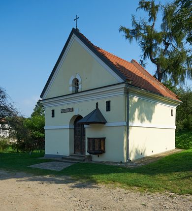 Zdjęcie nr 65: Kościół należy do zespołu dróżek Matki Boskiej, położnych w obrębie klasztoru w Kalwarii Zebrzydowskiej. Świątynia jest położna w centrum wsi, na wschód od głównej drogi, na placu otoczonym kamiennym murem z żeliwnym płotem, który od frontu ozdobiony jest figurami 12 apostołów, umieszczonymi na wysokich cokołach. Główne wejście na plac prowadzi przez bramę od zachodu, flankowaną dwoma filarami, na których ustawione są klasycystyczne wazony. Drugie wejście usytuowane jest od wschodu przez murowaną bramę, nakrytą daszkiem dwuspadowym, na którym ustawiona jest figura grającego na trąbie anioła. Trzecie wejście znajduje się od północy.

Kościół jest budowlą orientowaną, założoną na planie prostokąta, jednonawową, zamkniętą półkolistą absydą. Od zachodu przylega kruchta na planie prostokąta, zamkniętego z jednej strony półkoliście. Wewnątrz kościół dwupiętrowy. Na parterze część wschodnia świątyni podniesiona jest o siedem stopni, oddzielona od nawy trzema półkolistymi arkadami, wspartymi na czterech filarach i ustawionymi przed nimi półkolumnami, które wspierają pełne belkowanie, wyłamane na osiach. W przyłuczach płskorzeźbione główki aniołków. Na fryzie złocony napis: „EIA ADVOCATA NOSTRA OCVLOS MISERICORDES AD NOS CONVERTE ET IESVM BENEDICTV FRCTVM NOBIS OSTENDE”. Za środkową arkadą usytuowana jest niewielka, najstarsza część świątyni – Grób Matki Boskiej, na rzucie prostokąta, sklepiony krzyżowo. W ścianach bocznych nawy są półkoliście zamknięte wnęki na ołtarze. Od zachodu chór muzyczny wsparty jest na trzech arkadach filarowych. Wnętrze obiega drewniany ganek wsparty na metalowych wspornikach, a w części wschodniej i zachodniej na trzech murowanych arkadach. Podniebienie ganku zdobione jest geometrycznym stiukiem. W części nawowej świątyni znajduje się sklepienie kolebkowe z lunetami, w apsydzie hemisferyczne. Wnętrze doświetlone jest sześcioma małymi, okrągłymi oknami znajdującymi się na piętrze od strony północnej i południowej.

Fasada w dolnej części zaakcentowana jest przez monumentalną kruchtę w formie aediculi, założoną na rzucie prostokąta zamkniętego półkoliście. Ściany artykułowane są pięcioma półkolistymi arkadami, wspartymi na filarkach. Od zewnątrz osie ujęte są przez kanelowane kolumny, ustawione na wysokich cokołach, na tle pilastrów. Podpory wznoszą pełne belkowanie i wysunięty gzyms zdobiony kimationem i dekoracją kostkową. Nakrycie w formie kopuły półkolistej z latarnią. Belkowanie ozdobione jest dekoracją roślinną i główkami aniołków. Po bokach kruchty wysunięte są fragmenty muru oporowego do połowy wysokości fasady. Powyżej fasada flankowana przez dwie pary pilastrów z jońskimi kapitelami wspierającymi niepełne belkowanie. Pośrodku duże, półkoliste okno z metalową, dekoracyjną kratą. Szczyt trójkątny z oculusem pośrodku. Na szczycie ustawiona jest figura Najświętszej Marii Panny. Świątynia dookoła obwiedziona szerokim murem oporowym, nakrytym daszkiem, o ukośnych ścianach, flankowanych szkarpami, po sześć na każdej ścianie bocznej i dwoma na ścianie zachodniej oraz wschodniej. Powyżej elewacje ujęte pilastrami z kapitelami jońskimi wznoszącymi niepełne belkowanie. Na wschodniej ścianie półkolista apsyda, nakryta półkopułą. Kościół nakryty dachem siodłowym ze zdwojoną, wysoką latarnią pośrodku. Na narożach dachu ustawione wysokie obeliski na cokołach. 

 