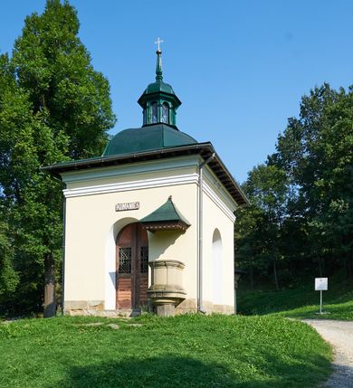 Zdjęcie nr 64: Kościół należy do zespołu dróżek Matki Boskiej, położnych w obrębie klasztoru w Kalwarii Zebrzydowskiej. Świątynia jest położna w centrum wsi, na wschód od głównej drogi, na placu otoczonym kamiennym murem z żeliwnym płotem, który od frontu ozdobiony jest figurami 12 apostołów, umieszczonymi na wysokich cokołach. Główne wejście na plac prowadzi przez bramę od zachodu, flankowaną dwoma filarami, na których ustawione są klasycystyczne wazony. Drugie wejście usytuowane jest od wschodu przez murowaną bramę, nakrytą daszkiem dwuspadowym, na którym ustawiona jest figura grającego na trąbie anioła. Trzecie wejście znajduje się od północy.

Kościół jest budowlą orientowaną, założoną na planie prostokąta, jednonawową, zamkniętą półkolistą absydą. Od zachodu przylega kruchta na planie prostokąta, zamkniętego z jednej strony półkoliście. Wewnątrz kościół dwupiętrowy. Na parterze część wschodnia świątyni podniesiona jest o siedem stopni, oddzielona od nawy trzema półkolistymi arkadami, wspartymi na czterech filarach i ustawionymi przed nimi półkolumnami, które wspierają pełne belkowanie, wyłamane na osiach. W przyłuczach płskorzeźbione główki aniołków. Na fryzie złocony napis: „EIA ADVOCATA NOSTRA OCVLOS MISERICORDES AD NOS CONVERTE ET IESVM BENEDICTV FRCTVM NOBIS OSTENDE”. Za środkową arkadą usytuowana jest niewielka, najstarsza część świątyni – Grób Matki Boskiej, na rzucie prostokąta, sklepiony krzyżowo. W ścianach bocznych nawy są półkoliście zamknięte wnęki na ołtarze. Od zachodu chór muzyczny wsparty jest na trzech arkadach filarowych. Wnętrze obiega drewniany ganek wsparty na metalowych wspornikach, a w części wschodniej i zachodniej na trzech murowanych arkadach. Podniebienie ganku zdobione jest geometrycznym stiukiem. W części nawowej świątyni znajduje się sklepienie kolebkowe z lunetami, w apsydzie hemisferyczne. Wnętrze doświetlone jest sześcioma małymi, okrągłymi oknami znajdującymi się na piętrze od strony północnej i południowej.

Fasada w dolnej części zaakcentowana jest przez monumentalną kruchtę w formie aediculi, założoną na rzucie prostokąta zamkniętego półkoliście. Ściany artykułowane są pięcioma półkolistymi arkadami, wspartymi na filarkach. Od zewnątrz osie ujęte są przez kanelowane kolumny, ustawione na wysokich cokołach, na tle pilastrów. Podpory wznoszą pełne belkowanie i wysunięty gzyms zdobiony kimationem i dekoracją kostkową. Nakrycie w formie kopuły półkolistej z latarnią. Belkowanie ozdobione jest dekoracją roślinną i główkami aniołków. Po bokach kruchty wysunięte są fragmenty muru oporowego do połowy wysokości fasady. Powyżej fasada flankowana przez dwie pary pilastrów z jońskimi kapitelami wspierającymi niepełne belkowanie. Pośrodku duże, półkoliste okno z metalową, dekoracyjną kratą. Szczyt trójkątny z oculusem pośrodku. Na szczycie ustawiona jest figura Najświętszej Marii Panny. Świątynia dookoła obwiedziona szerokim murem oporowym, nakrytym daszkiem, o ukośnych ścianach, flankowanych szkarpami, po sześć na każdej ścianie bocznej i dwoma na ścianie zachodniej oraz wschodniej. Powyżej elewacje ujęte pilastrami z kapitelami jońskimi wznoszącymi niepełne belkowanie. Na wschodniej ścianie półkolista apsyda, nakryta półkopułą. Kościół nakryty dachem siodłowym ze zdwojoną, wysoką latarnią pośrodku. Na narożach dachu ustawione wysokie obeliski na cokołach. 

 
