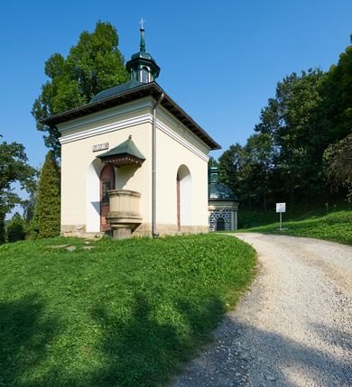 Zdjęcie nr 66: Kościół należy do zespołu dróżek Matki Boskiej, położnych w obrębie klasztoru w Kalwarii Zebrzydowskiej. Świątynia jest położna w centrum wsi, na wschód od głównej drogi, na placu otoczonym kamiennym murem z żeliwnym płotem, który od frontu ozdobiony jest figurami 12 apostołów, umieszczonymi na wysokich cokołach. Główne wejście na plac prowadzi przez bramę od zachodu, flankowaną dwoma filarami, na których ustawione są klasycystyczne wazony. Drugie wejście usytuowane jest od wschodu przez murowaną bramę, nakrytą daszkiem dwuspadowym, na którym ustawiona jest figura grającego na trąbie anioła. Trzecie wejście znajduje się od północy.

Kościół jest budowlą orientowaną, założoną na planie prostokąta, jednonawową, zamkniętą półkolistą absydą. Od zachodu przylega kruchta na planie prostokąta, zamkniętego z jednej strony półkoliście. Wewnątrz kościół dwupiętrowy. Na parterze część wschodnia świątyni podniesiona jest o siedem stopni, oddzielona od nawy trzema półkolistymi arkadami, wspartymi na czterech filarach i ustawionymi przed nimi półkolumnami, które wspierają pełne belkowanie, wyłamane na osiach. W przyłuczach płskorzeźbione główki aniołków. Na fryzie złocony napis: „EIA ADVOCATA NOSTRA OCVLOS MISERICORDES AD NOS CONVERTE ET IESVM BENEDICTV FRCTVM NOBIS OSTENDE”. Za środkową arkadą usytuowana jest niewielka, najstarsza część świątyni – Grób Matki Boskiej, na rzucie prostokąta, sklepiony krzyżowo. W ścianach bocznych nawy są półkoliście zamknięte wnęki na ołtarze. Od zachodu chór muzyczny wsparty jest na trzech arkadach filarowych. Wnętrze obiega drewniany ganek wsparty na metalowych wspornikach, a w części wschodniej i zachodniej na trzech murowanych arkadach. Podniebienie ganku zdobione jest geometrycznym stiukiem. W części nawowej świątyni znajduje się sklepienie kolebkowe z lunetami, w apsydzie hemisferyczne. Wnętrze doświetlone jest sześcioma małymi, okrągłymi oknami znajdującymi się na piętrze od strony północnej i południowej.

Fasada w dolnej części zaakcentowana jest przez monumentalną kruchtę w formie aediculi, założoną na rzucie prostokąta zamkniętego półkoliście. Ściany artykułowane są pięcioma półkolistymi arkadami, wspartymi na filarkach. Od zewnątrz osie ujęte są przez kanelowane kolumny, ustawione na wysokich cokołach, na tle pilastrów. Podpory wznoszą pełne belkowanie i wysunięty gzyms zdobiony kimationem i dekoracją kostkową. Nakrycie w formie kopuły półkolistej z latarnią. Belkowanie ozdobione jest dekoracją roślinną i główkami aniołków. Po bokach kruchty wysunięte są fragmenty muru oporowego do połowy wysokości fasady. Powyżej fasada flankowana przez dwie pary pilastrów z jońskimi kapitelami wspierającymi niepełne belkowanie. Pośrodku duże, półkoliste okno z metalową, dekoracyjną kratą. Szczyt trójkątny z oculusem pośrodku. Na szczycie ustawiona jest figura Najświętszej Marii Panny. Świątynia dookoła obwiedziona szerokim murem oporowym, nakrytym daszkiem, o ukośnych ścianach, flankowanych szkarpami, po sześć na każdej ścianie bocznej i dwoma na ścianie zachodniej oraz wschodniej. Powyżej elewacje ujęte pilastrami z kapitelami jońskimi wznoszącymi niepełne belkowanie. Na wschodniej ścianie półkolista apsyda, nakryta półkopułą. Kościół nakryty dachem siodłowym ze zdwojoną, wysoką latarnią pośrodku. Na narożach dachu ustawione wysokie obeliski na cokołach. 

 