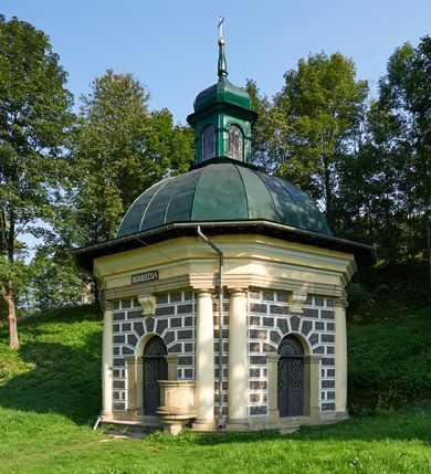 Zdjęcie nr 67: Kościół należy do zespołu dróżek Matki Boskiej, położnych w obrębie klasztoru w Kalwarii Zebrzydowskiej. Świątynia jest położna w centrum wsi, na wschód od głównej drogi, na placu otoczonym kamiennym murem z żeliwnym płotem, który od frontu ozdobiony jest figurami 12 apostołów, umieszczonymi na wysokich cokołach. Główne wejście na plac prowadzi przez bramę od zachodu, flankowaną dwoma filarami, na których ustawione są klasycystyczne wazony. Drugie wejście usytuowane jest od wschodu przez murowaną bramę, nakrytą daszkiem dwuspadowym, na którym ustawiona jest figura grającego na trąbie anioła. Trzecie wejście znajduje się od północy.

Kościół jest budowlą orientowaną, założoną na planie prostokąta, jednonawową, zamkniętą półkolistą absydą. Od zachodu przylega kruchta na planie prostokąta, zamkniętego z jednej strony półkoliście. Wewnątrz kościół dwupiętrowy. Na parterze część wschodnia świątyni podniesiona jest o siedem stopni, oddzielona od nawy trzema półkolistymi arkadami, wspartymi na czterech filarach i ustawionymi przed nimi półkolumnami, które wspierają pełne belkowanie, wyłamane na osiach. W przyłuczach płskorzeźbione główki aniołków. Na fryzie złocony napis: „EIA ADVOCATA NOSTRA OCVLOS MISERICORDES AD NOS CONVERTE ET IESVM BENEDICTV FRCTVM NOBIS OSTENDE”. Za środkową arkadą usytuowana jest niewielka, najstarsza część świątyni – Grób Matki Boskiej, na rzucie prostokąta, sklepiony krzyżowo. W ścianach bocznych nawy są półkoliście zamknięte wnęki na ołtarze. Od zachodu chór muzyczny wsparty jest na trzech arkadach filarowych. Wnętrze obiega drewniany ganek wsparty na metalowych wspornikach, a w części wschodniej i zachodniej na trzech murowanych arkadach. Podniebienie ganku zdobione jest geometrycznym stiukiem. W części nawowej świątyni znajduje się sklepienie kolebkowe z lunetami, w apsydzie hemisferyczne. Wnętrze doświetlone jest sześcioma małymi, okrągłymi oknami znajdującymi się na piętrze od strony północnej i południowej.

Fasada w dolnej części zaakcentowana jest przez monumentalną kruchtę w formie aediculi, założoną na rzucie prostokąta zamkniętego półkoliście. Ściany artykułowane są pięcioma półkolistymi arkadami, wspartymi na filarkach. Od zewnątrz osie ujęte są przez kanelowane kolumny, ustawione na wysokich cokołach, na tle pilastrów. Podpory wznoszą pełne belkowanie i wysunięty gzyms zdobiony kimationem i dekoracją kostkową. Nakrycie w formie kopuły półkolistej z latarnią. Belkowanie ozdobione jest dekoracją roślinną i główkami aniołków. Po bokach kruchty wysunięte są fragmenty muru oporowego do połowy wysokości fasady. Powyżej fasada flankowana przez dwie pary pilastrów z jońskimi kapitelami wspierającymi niepełne belkowanie. Pośrodku duże, półkoliste okno z metalową, dekoracyjną kratą. Szczyt trójkątny z oculusem pośrodku. Na szczycie ustawiona jest figura Najświętszej Marii Panny. Świątynia dookoła obwiedziona szerokim murem oporowym, nakrytym daszkiem, o ukośnych ścianach, flankowanych szkarpami, po sześć na każdej ścianie bocznej i dwoma na ścianie zachodniej oraz wschodniej. Powyżej elewacje ujęte pilastrami z kapitelami jońskimi wznoszącymi niepełne belkowanie. Na wschodniej ścianie półkolista apsyda, nakryta półkopułą. Kościół nakryty dachem siodłowym ze zdwojoną, wysoką latarnią pośrodku. Na narożach dachu ustawione wysokie obeliski na cokołach. 

 