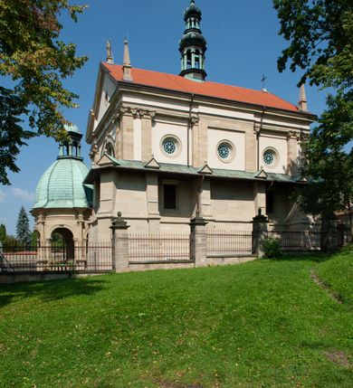 Zdjęcie nr 87: Kościół należy do zespołu dróżek Matki Boskiej, położnych w obrębie klasztoru w Kalwarii Zebrzydowskiej. Świątynia jest położna w centrum wsi, na wschód od głównej drogi, na placu otoczonym kamiennym murem z żeliwnym płotem, który od frontu ozdobiony jest figurami 12 apostołów, umieszczonymi na wysokich cokołach. Główne wejście na plac prowadzi przez bramę od zachodu, flankowaną dwoma filarami, na których ustawione są klasycystyczne wazony. Drugie wejście usytuowane jest od wschodu przez murowaną bramę, nakrytą daszkiem dwuspadowym, na którym ustawiona jest figura grającego na trąbie anioła. Trzecie wejście znajduje się od północy.

Kościół jest budowlą orientowaną, założoną na planie prostokąta, jednonawową, zamkniętą półkolistą absydą. Od zachodu przylega kruchta na planie prostokąta, zamkniętego z jednej strony półkoliście. Wewnątrz kościół dwupiętrowy. Na parterze część wschodnia świątyni podniesiona jest o siedem stopni, oddzielona od nawy trzema półkolistymi arkadami, wspartymi na czterech filarach i ustawionymi przed nimi półkolumnami, które wspierają pełne belkowanie, wyłamane na osiach. W przyłuczach płskorzeźbione główki aniołków. Na fryzie złocony napis: „EIA ADVOCATA NOSTRA OCVLOS MISERICORDES AD NOS CONVERTE ET IESVM BENEDICTV FRCTVM NOBIS OSTENDE”. Za środkową arkadą usytuowana jest niewielka, najstarsza część świątyni – Grób Matki Boskiej, na rzucie prostokąta, sklepiony krzyżowo. W ścianach bocznych nawy są półkoliście zamknięte wnęki na ołtarze. Od zachodu chór muzyczny wsparty jest na trzech arkadach filarowych. Wnętrze obiega drewniany ganek wsparty na metalowych wspornikach, a w części wschodniej i zachodniej na trzech murowanych arkadach. Podniebienie ganku zdobione jest geometrycznym stiukiem. W części nawowej świątyni znajduje się sklepienie kolebkowe z lunetami, w apsydzie hemisferyczne. Wnętrze doświetlone jest sześcioma małymi, okrągłymi oknami znajdującymi się na piętrze od strony północnej i południowej.

Fasada w dolnej części zaakcentowana jest przez monumentalną kruchtę w formie aediculi, założoną na rzucie prostokąta zamkniętego półkoliście. Ściany artykułowane są pięcioma półkolistymi arkadami, wspartymi na filarkach. Od zewnątrz osie ujęte są przez kanelowane kolumny, ustawione na wysokich cokołach, na tle pilastrów. Podpory wznoszą pełne belkowanie i wysunięty gzyms zdobiony kimationem i dekoracją kostkową. Nakrycie w formie kopuły półkolistej z latarnią. Belkowanie ozdobione jest dekoracją roślinną i główkami aniołków. Po bokach kruchty wysunięte są fragmenty muru oporowego do połowy wysokości fasady. Powyżej fasada flankowana przez dwie pary pilastrów z jońskimi kapitelami wspierającymi niepełne belkowanie. Pośrodku duże, półkoliste okno z metalową, dekoracyjną kratą. Szczyt trójkątny z oculusem pośrodku. Na szczycie ustawiona jest figura Najświętszej Marii Panny. Świątynia dookoła obwiedziona szerokim murem oporowym, nakrytym daszkiem, o ukośnych ścianach, flankowanych szkarpami, po sześć na każdej ścianie bocznej i dwoma na ścianie zachodniej oraz wschodniej. Powyżej elewacje ujęte pilastrami z kapitelami jońskimi wznoszącymi niepełne belkowanie. Na wschodniej ścianie półkolista apsyda, nakryta półkopułą. Kościół nakryty dachem siodłowym ze zdwojoną, wysoką latarnią pośrodku. Na narożach dachu ustawione wysokie obeliski na cokołach. 

 