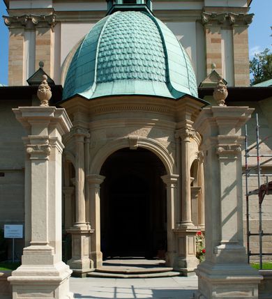 Zdjęcie nr 10: Kościół należy do zespołu dróżek Matki Boskiej, położnych w obrębie klasztoru w Kalwarii Zebrzydowskiej. Świątynia jest położna w centrum wsi, na wschód od głównej drogi, na placu otoczonym kamiennym murem z żeliwnym płotem, który od frontu ozdobiony jest figurami 12 apostołów, umieszczonymi na wysokich cokołach. Główne wejście na plac prowadzi przez bramę od zachodu, flankowaną dwoma filarami, na których ustawione są klasycystyczne wazony. Drugie wejście usytuowane jest od wschodu przez murowaną bramę, nakrytą daszkiem dwuspadowym, na którym ustawiona jest figura grającego na trąbie anioła. Trzecie wejście znajduje się od północy.

Kościół jest budowlą orientowaną, założoną na planie prostokąta, jednonawową, zamkniętą półkolistą absydą. Od zachodu przylega kruchta na planie prostokąta, zamkniętego z jednej strony półkoliście. Wewnątrz kościół dwupiętrowy. Na parterze część wschodnia świątyni podniesiona jest o siedem stopni, oddzielona od nawy trzema półkolistymi arkadami, wspartymi na czterech filarach i ustawionymi przed nimi półkolumnami, które wspierają pełne belkowanie, wyłamane na osiach. W przyłuczach płskorzeźbione główki aniołków. Na fryzie złocony napis: „EIA ADVOCATA NOSTRA OCVLOS MISERICORDES AD NOS CONVERTE ET IESVM BENEDICTV FRCTVM NOBIS OSTENDE”. Za środkową arkadą usytuowana jest niewielka, najstarsza część świątyni – Grób Matki Boskiej, na rzucie prostokąta, sklepiony krzyżowo. W ścianach bocznych nawy są półkoliście zamknięte wnęki na ołtarze. Od zachodu chór muzyczny wsparty jest na trzech arkadach filarowych. Wnętrze obiega drewniany ganek wsparty na metalowych wspornikach, a w części wschodniej i zachodniej na trzech murowanych arkadach. Podniebienie ganku zdobione jest geometrycznym stiukiem. W części nawowej świątyni znajduje się sklepienie kolebkowe z lunetami, w apsydzie hemisferyczne. Wnętrze doświetlone jest sześcioma małymi, okrągłymi oknami znajdującymi się na piętrze od strony północnej i południowej.

Fasada w dolnej części zaakcentowana jest przez monumentalną kruchtę w formie aediculi, założoną na rzucie prostokąta zamkniętego półkoliście. Ściany artykułowane są pięcioma półkolistymi arkadami, wspartymi na filarkach. Od zewnątrz osie ujęte są przez kanelowane kolumny, ustawione na wysokich cokołach, na tle pilastrów. Podpory wznoszą pełne belkowanie i wysunięty gzyms zdobiony kimationem i dekoracją kostkową. Nakrycie w formie kopuły półkolistej z latarnią. Belkowanie ozdobione jest dekoracją roślinną i główkami aniołków. Po bokach kruchty wysunięte są fragmenty muru oporowego do połowy wysokości fasady. Powyżej fasada flankowana przez dwie pary pilastrów z jońskimi kapitelami wspierającymi niepełne belkowanie. Pośrodku duże, półkoliste okno z metalową, dekoracyjną kratą. Szczyt trójkątny z oculusem pośrodku. Na szczycie ustawiona jest figura Najświętszej Marii Panny. Świątynia dookoła obwiedziona szerokim murem oporowym, nakrytym daszkiem, o ukośnych ścianach, flankowanych szkarpami, po sześć na każdej ścianie bocznej i dwoma na ścianie zachodniej oraz wschodniej. Powyżej elewacje ujęte pilastrami z kapitelami jońskimi wznoszącymi niepełne belkowanie. Na wschodniej ścianie półkolista apsyda, nakryta półkopułą. Kościół nakryty dachem siodłowym ze zdwojoną, wysoką latarnią pośrodku. Na narożach dachu ustawione wysokie obeliski na cokołach. 

 