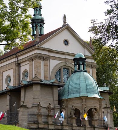 Zdjęcie nr 57: Kościół należy do zespołu dróżek Matki Boskiej, położnych w obrębie klasztoru w Kalwarii Zebrzydowskiej. Świątynia jest położna w centrum wsi, na wschód od głównej drogi, na placu otoczonym kamiennym murem z żeliwnym płotem, który od frontu ozdobiony jest figurami 12 apostołów, umieszczonymi na wysokich cokołach. Główne wejście na plac prowadzi przez bramę od zachodu, flankowaną dwoma filarami, na których ustawione są klasycystyczne wazony. Drugie wejście usytuowane jest od wschodu przez murowaną bramę, nakrytą daszkiem dwuspadowym, na którym ustawiona jest figura grającego na trąbie anioła. Trzecie wejście znajduje się od północy.

Kościół jest budowlą orientowaną, założoną na planie prostokąta, jednonawową, zamkniętą półkolistą absydą. Od zachodu przylega kruchta na planie prostokąta, zamkniętego z jednej strony półkoliście. Wewnątrz kościół dwupiętrowy. Na parterze część wschodnia świątyni podniesiona jest o siedem stopni, oddzielona od nawy trzema półkolistymi arkadami, wspartymi na czterech filarach i ustawionymi przed nimi półkolumnami, które wspierają pełne belkowanie, wyłamane na osiach. W przyłuczach płskorzeźbione główki aniołków. Na fryzie złocony napis: „EIA ADVOCATA NOSTRA OCVLOS MISERICORDES AD NOS CONVERTE ET IESVM BENEDICTV FRCTVM NOBIS OSTENDE”. Za środkową arkadą usytuowana jest niewielka, najstarsza część świątyni – Grób Matki Boskiej, na rzucie prostokąta, sklepiony krzyżowo. W ścianach bocznych nawy są półkoliście zamknięte wnęki na ołtarze. Od zachodu chór muzyczny wsparty jest na trzech arkadach filarowych. Wnętrze obiega drewniany ganek wsparty na metalowych wspornikach, a w części wschodniej i zachodniej na trzech murowanych arkadach. Podniebienie ganku zdobione jest geometrycznym stiukiem. W części nawowej świątyni znajduje się sklepienie kolebkowe z lunetami, w apsydzie hemisferyczne. Wnętrze doświetlone jest sześcioma małymi, okrągłymi oknami znajdującymi się na piętrze od strony północnej i południowej.

Fasada w dolnej części zaakcentowana jest przez monumentalną kruchtę w formie aediculi, założoną na rzucie prostokąta zamkniętego półkoliście. Ściany artykułowane są pięcioma półkolistymi arkadami, wspartymi na filarkach. Od zewnątrz osie ujęte są przez kanelowane kolumny, ustawione na wysokich cokołach, na tle pilastrów. Podpory wznoszą pełne belkowanie i wysunięty gzyms zdobiony kimationem i dekoracją kostkową. Nakrycie w formie kopuły półkolistej z latarnią. Belkowanie ozdobione jest dekoracją roślinną i główkami aniołków. Po bokach kruchty wysunięte są fragmenty muru oporowego do połowy wysokości fasady. Powyżej fasada flankowana przez dwie pary pilastrów z jońskimi kapitelami wspierającymi niepełne belkowanie. Pośrodku duże, półkoliste okno z metalową, dekoracyjną kratą. Szczyt trójkątny z oculusem pośrodku. Na szczycie ustawiona jest figura Najświętszej Marii Panny. Świątynia dookoła obwiedziona szerokim murem oporowym, nakrytym daszkiem, o ukośnych ścianach, flankowanych szkarpami, po sześć na każdej ścianie bocznej i dwoma na ścianie zachodniej oraz wschodniej. Powyżej elewacje ujęte pilastrami z kapitelami jońskimi wznoszącymi niepełne belkowanie. Na wschodniej ścianie półkolista apsyda, nakryta półkopułą. Kościół nakryty dachem siodłowym ze zdwojoną, wysoką latarnią pośrodku. Na narożach dachu ustawione wysokie obeliski na cokołach. 

 