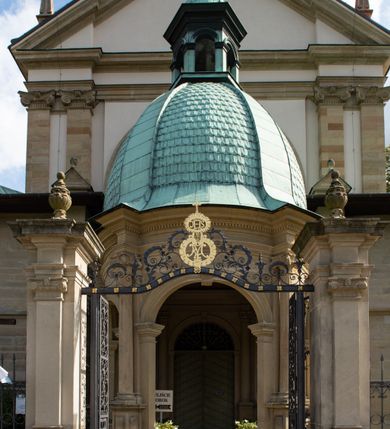 Zdjęcie nr 12: Kościół należy do zespołu dróżek Matki Boskiej, położnych w obrębie klasztoru w Kalwarii Zebrzydowskiej. Świątynia jest położna w centrum wsi, na wschód od głównej drogi, na placu otoczonym kamiennym murem z żeliwnym płotem, który od frontu ozdobiony jest figurami 12 apostołów, umieszczonymi na wysokich cokołach. Główne wejście na plac prowadzi przez bramę od zachodu, flankowaną dwoma filarami, na których ustawione są klasycystyczne wazony. Drugie wejście usytuowane jest od wschodu przez murowaną bramę, nakrytą daszkiem dwuspadowym, na którym ustawiona jest figura grającego na trąbie anioła. Trzecie wejście znajduje się od północy.

Kościół jest budowlą orientowaną, założoną na planie prostokąta, jednonawową, zamkniętą półkolistą absydą. Od zachodu przylega kruchta na planie prostokąta, zamkniętego z jednej strony półkoliście. Wewnątrz kościół dwupiętrowy. Na parterze część wschodnia świątyni podniesiona jest o siedem stopni, oddzielona od nawy trzema półkolistymi arkadami, wspartymi na czterech filarach i ustawionymi przed nimi półkolumnami, które wspierają pełne belkowanie, wyłamane na osiach. W przyłuczach płskorzeźbione główki aniołków. Na fryzie złocony napis: „EIA ADVOCATA NOSTRA OCVLOS MISERICORDES AD NOS CONVERTE ET IESVM BENEDICTV FRCTVM NOBIS OSTENDE”. Za środkową arkadą usytuowana jest niewielka, najstarsza część świątyni – Grób Matki Boskiej, na rzucie prostokąta, sklepiony krzyżowo. W ścianach bocznych nawy są półkoliście zamknięte wnęki na ołtarze. Od zachodu chór muzyczny wsparty jest na trzech arkadach filarowych. Wnętrze obiega drewniany ganek wsparty na metalowych wspornikach, a w części wschodniej i zachodniej na trzech murowanych arkadach. Podniebienie ganku zdobione jest geometrycznym stiukiem. W części nawowej świątyni znajduje się sklepienie kolebkowe z lunetami, w apsydzie hemisferyczne. Wnętrze doświetlone jest sześcioma małymi, okrągłymi oknami znajdującymi się na piętrze od strony północnej i południowej.

Fasada w dolnej części zaakcentowana jest przez monumentalną kruchtę w formie aediculi, założoną na rzucie prostokąta zamkniętego półkoliście. Ściany artykułowane są pięcioma półkolistymi arkadami, wspartymi na filarkach. Od zewnątrz osie ujęte są przez kanelowane kolumny, ustawione na wysokich cokołach, na tle pilastrów. Podpory wznoszą pełne belkowanie i wysunięty gzyms zdobiony kimationem i dekoracją kostkową. Nakrycie w formie kopuły półkolistej z latarnią. Belkowanie ozdobione jest dekoracją roślinną i główkami aniołków. Po bokach kruchty wysunięte są fragmenty muru oporowego do połowy wysokości fasady. Powyżej fasada flankowana przez dwie pary pilastrów z jońskimi kapitelami wspierającymi niepełne belkowanie. Pośrodku duże, półkoliste okno z metalową, dekoracyjną kratą. Szczyt trójkątny z oculusem pośrodku. Na szczycie ustawiona jest figura Najświętszej Marii Panny. Świątynia dookoła obwiedziona szerokim murem oporowym, nakrytym daszkiem, o ukośnych ścianach, flankowanych szkarpami, po sześć na każdej ścianie bocznej i dwoma na ścianie zachodniej oraz wschodniej. Powyżej elewacje ujęte pilastrami z kapitelami jońskimi wznoszącymi niepełne belkowanie. Na wschodniej ścianie półkolista apsyda, nakryta półkopułą. Kościół nakryty dachem siodłowym ze zdwojoną, wysoką latarnią pośrodku. Na narożach dachu ustawione wysokie obeliski na cokołach. 

 