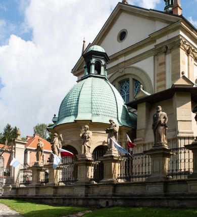 Zdjęcie nr 19: Kościół należy do zespołu dróżek Matki Boskiej, położnych w obrębie klasztoru w Kalwarii Zebrzydowskiej. Świątynia jest położna w centrum wsi, na wschód od głównej drogi, na placu otoczonym kamiennym murem z żeliwnym płotem, który od frontu ozdobiony jest figurami 12 apostołów, umieszczonymi na wysokich cokołach. Główne wejście na plac prowadzi przez bramę od zachodu, flankowaną dwoma filarami, na których ustawione są klasycystyczne wazony. Drugie wejście usytuowane jest od wschodu przez murowaną bramę, nakrytą daszkiem dwuspadowym, na którym ustawiona jest figura grającego na trąbie anioła. Trzecie wejście znajduje się od północy.

Kościół jest budowlą orientowaną, założoną na planie prostokąta, jednonawową, zamkniętą półkolistą absydą. Od zachodu przylega kruchta na planie prostokąta, zamkniętego z jednej strony półkoliście. Wewnątrz kościół dwupiętrowy. Na parterze część wschodnia świątyni podniesiona jest o siedem stopni, oddzielona od nawy trzema półkolistymi arkadami, wspartymi na czterech filarach i ustawionymi przed nimi półkolumnami, które wspierają pełne belkowanie, wyłamane na osiach. W przyłuczach płskorzeźbione główki aniołków. Na fryzie złocony napis: „EIA ADVOCATA NOSTRA OCVLOS MISERICORDES AD NOS CONVERTE ET IESVM BENEDICTV FRCTVM NOBIS OSTENDE”. Za środkową arkadą usytuowana jest niewielka, najstarsza część świątyni – Grób Matki Boskiej, na rzucie prostokąta, sklepiony krzyżowo. W ścianach bocznych nawy są półkoliście zamknięte wnęki na ołtarze. Od zachodu chór muzyczny wsparty jest na trzech arkadach filarowych. Wnętrze obiega drewniany ganek wsparty na metalowych wspornikach, a w części wschodniej i zachodniej na trzech murowanych arkadach. Podniebienie ganku zdobione jest geometrycznym stiukiem. W części nawowej świątyni znajduje się sklepienie kolebkowe z lunetami, w apsydzie hemisferyczne. Wnętrze doświetlone jest sześcioma małymi, okrągłymi oknami znajdującymi się na piętrze od strony północnej i południowej.

Fasada w dolnej części zaakcentowana jest przez monumentalną kruchtę w formie aediculi, założoną na rzucie prostokąta zamkniętego półkoliście. Ściany artykułowane są pięcioma półkolistymi arkadami, wspartymi na filarkach. Od zewnątrz osie ujęte są przez kanelowane kolumny, ustawione na wysokich cokołach, na tle pilastrów. Podpory wznoszą pełne belkowanie i wysunięty gzyms zdobiony kimationem i dekoracją kostkową. Nakrycie w formie kopuły półkolistej z latarnią. Belkowanie ozdobione jest dekoracją roślinną i główkami aniołków. Po bokach kruchty wysunięte są fragmenty muru oporowego do połowy wysokości fasady. Powyżej fasada flankowana przez dwie pary pilastrów z jońskimi kapitelami wspierającymi niepełne belkowanie. Pośrodku duże, półkoliste okno z metalową, dekoracyjną kratą. Szczyt trójkątny z oculusem pośrodku. Na szczycie ustawiona jest figura Najświętszej Marii Panny. Świątynia dookoła obwiedziona szerokim murem oporowym, nakrytym daszkiem, o ukośnych ścianach, flankowanych szkarpami, po sześć na każdej ścianie bocznej i dwoma na ścianie zachodniej oraz wschodniej. Powyżej elewacje ujęte pilastrami z kapitelami jońskimi wznoszącymi niepełne belkowanie. Na wschodniej ścianie półkolista apsyda, nakryta półkopułą. Kościół nakryty dachem siodłowym ze zdwojoną, wysoką latarnią pośrodku. Na narożach dachu ustawione wysokie obeliski na cokołach. 

 