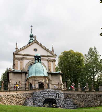 Zdjęcie nr 86: Kościół należy do zespołu dróżek Matki Boskiej, położnych w obrębie klasztoru w Kalwarii Zebrzydowskiej. Świątynia jest położna w centrum wsi, na wschód od głównej drogi, na placu otoczonym kamiennym murem z żeliwnym płotem, który od frontu ozdobiony jest figurami 12 apostołów, umieszczonymi na wysokich cokołach. Główne wejście na plac prowadzi przez bramę od zachodu, flankowaną dwoma filarami, na których ustawione są klasycystyczne wazony. Drugie wejście usytuowane jest od wschodu przez murowaną bramę, nakrytą daszkiem dwuspadowym, na którym ustawiona jest figura grającego na trąbie anioła. Trzecie wejście znajduje się od północy.

Kościół jest budowlą orientowaną, założoną na planie prostokąta, jednonawową, zamkniętą półkolistą absydą. Od zachodu przylega kruchta na planie prostokąta, zamkniętego z jednej strony półkoliście. Wewnątrz kościół dwupiętrowy. Na parterze część wschodnia świątyni podniesiona jest o siedem stopni, oddzielona od nawy trzema półkolistymi arkadami, wspartymi na czterech filarach i ustawionymi przed nimi półkolumnami, które wspierają pełne belkowanie, wyłamane na osiach. W przyłuczach płskorzeźbione główki aniołków. Na fryzie złocony napis: „EIA ADVOCATA NOSTRA OCVLOS MISERICORDES AD NOS CONVERTE ET IESVM BENEDICTV FRCTVM NOBIS OSTENDE”. Za środkową arkadą usytuowana jest niewielka, najstarsza część świątyni – Grób Matki Boskiej, na rzucie prostokąta, sklepiony krzyżowo. W ścianach bocznych nawy są półkoliście zamknięte wnęki na ołtarze. Od zachodu chór muzyczny wsparty jest na trzech arkadach filarowych. Wnętrze obiega drewniany ganek wsparty na metalowych wspornikach, a w części wschodniej i zachodniej na trzech murowanych arkadach. Podniebienie ganku zdobione jest geometrycznym stiukiem. W części nawowej świątyni znajduje się sklepienie kolebkowe z lunetami, w apsydzie hemisferyczne. Wnętrze doświetlone jest sześcioma małymi, okrągłymi oknami znajdującymi się na piętrze od strony północnej i południowej.

Fasada w dolnej części zaakcentowana jest przez monumentalną kruchtę w formie aediculi, założoną na rzucie prostokąta zamkniętego półkoliście. Ściany artykułowane są pięcioma półkolistymi arkadami, wspartymi na filarkach. Od zewnątrz osie ujęte są przez kanelowane kolumny, ustawione na wysokich cokołach, na tle pilastrów. Podpory wznoszą pełne belkowanie i wysunięty gzyms zdobiony kimationem i dekoracją kostkową. Nakrycie w formie kopuły półkolistej z latarnią. Belkowanie ozdobione jest dekoracją roślinną i główkami aniołków. Po bokach kruchty wysunięte są fragmenty muru oporowego do połowy wysokości fasady. Powyżej fasada flankowana przez dwie pary pilastrów z jońskimi kapitelami wspierającymi niepełne belkowanie. Pośrodku duże, półkoliste okno z metalową, dekoracyjną kratą. Szczyt trójkątny z oculusem pośrodku. Na szczycie ustawiona jest figura Najświętszej Marii Panny. Świątynia dookoła obwiedziona szerokim murem oporowym, nakrytym daszkiem, o ukośnych ścianach, flankowanych szkarpami, po sześć na każdej ścianie bocznej i dwoma na ścianie zachodniej oraz wschodniej. Powyżej elewacje ujęte pilastrami z kapitelami jońskimi wznoszącymi niepełne belkowanie. Na wschodniej ścianie półkolista apsyda, nakryta półkopułą. Kościół nakryty dachem siodłowym ze zdwojoną, wysoką latarnią pośrodku. Na narożach dachu ustawione wysokie obeliski na cokołach. 

 