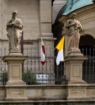 Zdjęcie nr 70: Kościół należy do zespołu dróżek Matki Boskiej, położnych w obrębie klasztoru w Kalwarii Zebrzydowskiej. Świątynia jest położna w centrum wsi, na wschód od głównej drogi, na placu otoczonym kamiennym murem z żeliwnym płotem, który od frontu ozdobiony jest figurami 12 apostołów, umieszczonymi na wysokich cokołach. Główne wejście na plac prowadzi przez bramę od zachodu, flankowaną dwoma filarami, na których ustawione są klasycystyczne wazony. Drugie wejście usytuowane jest od wschodu przez murowaną bramę, nakrytą daszkiem dwuspadowym, na którym ustawiona jest figura grającego na trąbie anioła. Trzecie wejście znajduje się od północy.

Kościół jest budowlą orientowaną, założoną na planie prostokąta, jednonawową, zamkniętą półkolistą absydą. Od zachodu przylega kruchta na planie prostokąta, zamkniętego z jednej strony półkoliście. Wewnątrz kościół dwupiętrowy. Na parterze część wschodnia świątyni podniesiona jest o siedem stopni, oddzielona od nawy trzema półkolistymi arkadami, wspartymi na czterech filarach i ustawionymi przed nimi półkolumnami, które wspierają pełne belkowanie, wyłamane na osiach. W przyłuczach płskorzeźbione główki aniołków. Na fryzie złocony napis: „EIA ADVOCATA NOSTRA OCVLOS MISERICORDES AD NOS CONVERTE ET IESVM BENEDICTV FRCTVM NOBIS OSTENDE”. Za środkową arkadą usytuowana jest niewielka, najstarsza część świątyni – Grób Matki Boskiej, na rzucie prostokąta, sklepiony krzyżowo. W ścianach bocznych nawy są półkoliście zamknięte wnęki na ołtarze. Od zachodu chór muzyczny wsparty jest na trzech arkadach filarowych. Wnętrze obiega drewniany ganek wsparty na metalowych wspornikach, a w części wschodniej i zachodniej na trzech murowanych arkadach. Podniebienie ganku zdobione jest geometrycznym stiukiem. W części nawowej świątyni znajduje się sklepienie kolebkowe z lunetami, w apsydzie hemisferyczne. Wnętrze doświetlone jest sześcioma małymi, okrągłymi oknami znajdującymi się na piętrze od strony północnej i południowej.

Fasada w dolnej części zaakcentowana jest przez monumentalną kruchtę w formie aediculi, założoną na rzucie prostokąta zamkniętego półkoliście. Ściany artykułowane są pięcioma półkolistymi arkadami, wspartymi na filarkach. Od zewnątrz osie ujęte są przez kanelowane kolumny, ustawione na wysokich cokołach, na tle pilastrów. Podpory wznoszą pełne belkowanie i wysunięty gzyms zdobiony kimationem i dekoracją kostkową. Nakrycie w formie kopuły półkolistej z latarnią. Belkowanie ozdobione jest dekoracją roślinną i główkami aniołków. Po bokach kruchty wysunięte są fragmenty muru oporowego do połowy wysokości fasady. Powyżej fasada flankowana przez dwie pary pilastrów z jońskimi kapitelami wspierającymi niepełne belkowanie. Pośrodku duże, półkoliste okno z metalową, dekoracyjną kratą. Szczyt trójkątny z oculusem pośrodku. Na szczycie ustawiona jest figura Najświętszej Marii Panny. Świątynia dookoła obwiedziona szerokim murem oporowym, nakrytym daszkiem, o ukośnych ścianach, flankowanych szkarpami, po sześć na każdej ścianie bocznej i dwoma na ścianie zachodniej oraz wschodniej. Powyżej elewacje ujęte pilastrami z kapitelami jońskimi wznoszącymi niepełne belkowanie. Na wschodniej ścianie półkolista apsyda, nakryta półkopułą. Kościół nakryty dachem siodłowym ze zdwojoną, wysoką latarnią pośrodku. Na narożach dachu ustawione wysokie obeliski na cokołach. 

 