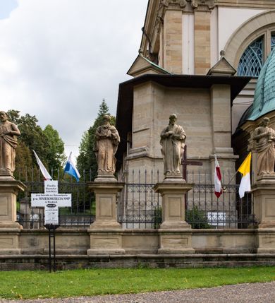 Zdjęcie nr 71: Kościół należy do zespołu dróżek Matki Boskiej, położnych w obrębie klasztoru w Kalwarii Zebrzydowskiej. Świątynia jest położna w centrum wsi, na wschód od głównej drogi, na placu otoczonym kamiennym murem z żeliwnym płotem, który od frontu ozdobiony jest figurami 12 apostołów, umieszczonymi na wysokich cokołach. Główne wejście na plac prowadzi przez bramę od zachodu, flankowaną dwoma filarami, na których ustawione są klasycystyczne wazony. Drugie wejście usytuowane jest od wschodu przez murowaną bramę, nakrytą daszkiem dwuspadowym, na którym ustawiona jest figura grającego na trąbie anioła. Trzecie wejście znajduje się od północy.

Kościół jest budowlą orientowaną, założoną na planie prostokąta, jednonawową, zamkniętą półkolistą absydą. Od zachodu przylega kruchta na planie prostokąta, zamkniętego z jednej strony półkoliście. Wewnątrz kościół dwupiętrowy. Na parterze część wschodnia świątyni podniesiona jest o siedem stopni, oddzielona od nawy trzema półkolistymi arkadami, wspartymi na czterech filarach i ustawionymi przed nimi półkolumnami, które wspierają pełne belkowanie, wyłamane na osiach. W przyłuczach płskorzeźbione główki aniołków. Na fryzie złocony napis: „EIA ADVOCATA NOSTRA OCVLOS MISERICORDES AD NOS CONVERTE ET IESVM BENEDICTV FRCTVM NOBIS OSTENDE”. Za środkową arkadą usytuowana jest niewielka, najstarsza część świątyni – Grób Matki Boskiej, na rzucie prostokąta, sklepiony krzyżowo. W ścianach bocznych nawy są półkoliście zamknięte wnęki na ołtarze. Od zachodu chór muzyczny wsparty jest na trzech arkadach filarowych. Wnętrze obiega drewniany ganek wsparty na metalowych wspornikach, a w części wschodniej i zachodniej na trzech murowanych arkadach. Podniebienie ganku zdobione jest geometrycznym stiukiem. W części nawowej świątyni znajduje się sklepienie kolebkowe z lunetami, w apsydzie hemisferyczne. Wnętrze doświetlone jest sześcioma małymi, okrągłymi oknami znajdującymi się na piętrze od strony północnej i południowej.

Fasada w dolnej części zaakcentowana jest przez monumentalną kruchtę w formie aediculi, założoną na rzucie prostokąta zamkniętego półkoliście. Ściany artykułowane są pięcioma półkolistymi arkadami, wspartymi na filarkach. Od zewnątrz osie ujęte są przez kanelowane kolumny, ustawione na wysokich cokołach, na tle pilastrów. Podpory wznoszą pełne belkowanie i wysunięty gzyms zdobiony kimationem i dekoracją kostkową. Nakrycie w formie kopuły półkolistej z latarnią. Belkowanie ozdobione jest dekoracją roślinną i główkami aniołków. Po bokach kruchty wysunięte są fragmenty muru oporowego do połowy wysokości fasady. Powyżej fasada flankowana przez dwie pary pilastrów z jońskimi kapitelami wspierającymi niepełne belkowanie. Pośrodku duże, półkoliste okno z metalową, dekoracyjną kratą. Szczyt trójkątny z oculusem pośrodku. Na szczycie ustawiona jest figura Najświętszej Marii Panny. Świątynia dookoła obwiedziona szerokim murem oporowym, nakrytym daszkiem, o ukośnych ścianach, flankowanych szkarpami, po sześć na każdej ścianie bocznej i dwoma na ścianie zachodniej oraz wschodniej. Powyżej elewacje ujęte pilastrami z kapitelami jońskimi wznoszącymi niepełne belkowanie. Na wschodniej ścianie półkolista apsyda, nakryta półkopułą. Kościół nakryty dachem siodłowym ze zdwojoną, wysoką latarnią pośrodku. Na narożach dachu ustawione wysokie obeliski na cokołach. 

 