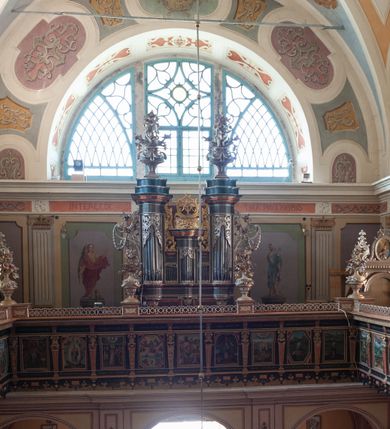 Zdjęcie nr 3: Organy architektoniczne, pięcioosiowe, jednokondygnacyjne na cokole. Oś środkowa i skrajne wydzielone wielobocznymi ryzalitami, środkowa dwukrotnie niższa, flankowana dwiema niższymi. Wszystkie osie z prześwitami na piszczałki w formie stojącego prostokąta, zwieńczone belkowaniem. Na belkowaniu osi środkowej szczyt z monogramem maryjnym, ujęty wiciami roślinnymi wychodzącymi z osi wewnętrznych. Prześwity w górnej partii wypełnione ażurowym ornamentem roślinnym. Organy ujęte uszami utworzonymi z wolut i zawieszonych na nich ukwieconych gałązek i kampanuli. Na osiach bocznych ustawione wysokie wazony z kwiatami. Struktura polichromowana w kolorze zielonym, profilowania na czerwono, marmoryzowana, ornamentyka złocona i srebrzona.