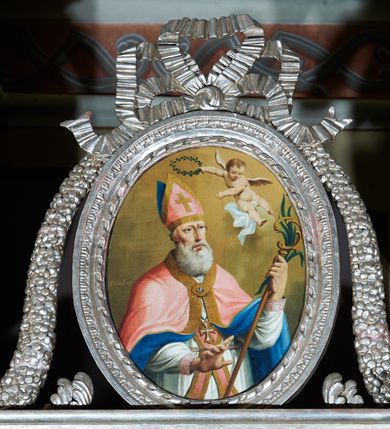 Zdjęcie nr 8: Ołtarz ustawiony na piętrze kościoła. Nastawa jednokondygnacyjna, trójosiowa, ażurowa z dostawionymi po bokach małymi ołtarzykami. Tabernakulum w formie prostopadłościennej skrzynki o wykroju wklęsło-wypukłym, ustawione na cokole i zamknięte profilowanym, wyłamanym gzymsem. Ścianki boczne ustawione pod skosem, wklęsłe, zdobione ukośną, ażurową dekoracją ornamentalną składającą się z kratki, wolut i liści akantu. Ścianka frontowa, wypukła flankowana parą ukośnie ustawionych pilastrów, których trzony zdobione są spływami wolutowymi oraz kwiatowymi. Pośrodku wnęka z metalowym, ruchomym i obrotowym (?) wsadem, który na jednej ze ścianek zdobiony jest płyciną w kształcie stojącego prostokąta zamkniętego łukiem wklęsło-wypukłym z uskokami z przedstawieniem Baranka Bożego na księdze zamkniętej siedmioma pieczęciami, liter alfa i omega oraz powyżej gołębicy Ducha Świętego. Płycina ujęta kimationem, w przyłuczach winne grona. 

Nastawa wsparta na wysokim cokole. Oś główna flankowana parą krótkich pilastrów o kanelowanych trzonach i kompozytowych kapitelach. Przed nimi ustawiona ukośnie para kolumn o dłuższych trzonach, wspartych na pojedynczych, oddzielnych cokołach. Podpory wspólnie wspierają przerwane belkowanie. Kolumny mają bazy, kanelowane trzony i kompozytowe kapitele. W polu głównym znajduje się głęboka wnęka ujęta szeroką, dekoracyjną ramą w kształcie stojącego prostokąta z uszakami, zamknięta łukiem dwuramiennym. Wewnątrz ustawiona jest figura Matki Boskiej Niepokalanie Poczętej na czerwonym materiałowym tle. Dokoła wnęki bogata dekoracja utworzona z gałązek róż i obłoków. Nad wnęką okrągły medalion, ozdobiony u góry karbowaną wstęgą z napisem: „«Astitit / Regina a dex»/Tris tuis in ve/Stitu de[a]vrato / Psal 44 ver 11”. Pomiędzy osią główną, a flankującymi ją pilastrami prześwity. 

Zwieńczenie w formie monumentalnej glorii z wpisanym w polu otokiem z obłoków. Wewnątrz rzeźbiona Trójca Święta oraz cztery uskrzydlone główki anielskie. Na belkowaniu usadzone dwie pary muzykujących aniołów oraz jedna para wysokich wazonów z bujnymi kwiatami. 

W osiach bocznych, w dolnej części cokołowej bramki ujęte szerokimi, kanelowanymi pilastrami podtrzymującymi belkowanie. Przejścia w kształcie stojących prostokątów, zamkniętych półkoliście, flankowane filarkami. W górnej części osi bocznych na niskim podeście ustawione są wysokie, wąskie kanelowane filary ze stylizowanymi jońskimi kapitelami, na których na postumentach w kształcie stylizowanej egipskiej głowicy ustawione są figury: króla Saula z małym Dawidem w lewej osi oraz króla Dawida w prawej osi bocznej. Filary ujęte są po bokach ażurową snycerską dekoracją złożoną z esownic zdobionych cekinami oraz dekoracji roślinnej utworzonej z liści stylizowanego akantu oraz kwiatów. 

Po bokach ołtarza dostawiona jest para małych ołtarzyków, jednokondygnacyjnych i jednoosiowych. Mensy sarkofagowe o kształcie niesymetrycznym: prawy bok przylega do ściany; w polu dwie fornirowane płyciny. Nastawy ołtarzowe, symetryczne, wsparte na łamanym cokole, ujęte parą pilastrów oraz parą kolumn z kanelowanymi i złoconymi trzonami oraz o kompozytowych kapitelach. Podpory wspierają wyłamane belkowania i silnie profilowane gzymsy. Ołtarze zwieńczone są promienistymi gloriami, w których w niebieskim polu, otoczonym obłokami znajduje się: w ołtarzyku po lewej stornie kwiat róży, a w ołtarzyku po prawej stronie gwiazda. W polach centralnych w ramach w kształcie stojących prostokątów z uszakami o wklęsłych górnych narożach umieszczone są obrazy. W ołtarzyku po lewej stronie obraz przedstawiający „Pokłon pasterzy”, a w ołtarzyku po prawej stronie obraz „Pokłon Trzech Króli”. 

Struktura polichromowana w kolorze jasnoniebieskim; ornamentyka, detale i profilowania złocone oraz srebrzone. 


