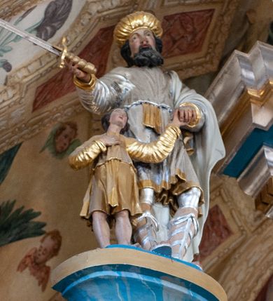 Zdjęcie nr 1: Rzeźba przedstawiająca króla Saula z Dawidem. Mężczyźni ukazani w postawie stojącej, trzymający się za lewe dłonie. Dawid sięgający do wysokości pasa Saula ustawiony przy jego prawym boku. Król w prawej dłoni trzyma miecz, a Dawid prawą dłoń składa na piersi. Twarz Saula szeroka z długim nosem, delikatnie rozchylonymi ustami, okolona średniej długości, czarną brodą oraz czarnymi włosami. Ubrany jest w srebrną tunikę, przewiązaną złotym pasem oraz biały płaszcz założony na lewe ramię; na głowie ma złoty turban, a na stopach wysokie rzymskie sandały. Dawid ubrany jest w złoconą tunikę z długimi rękawami. Polichromia w odsłoniętych partiach ciała naturalistyczna, szaty i detale złocone i srebrzone. 

