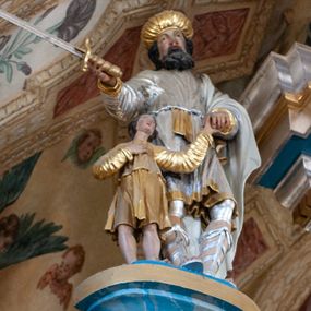 Zdjęcie nr 1: Rzeźba przedstawiająca króla Saula z Dawidem. Mężczyźni ukazani w postawie stojącej, trzymający się za lewe dłonie. Dawid sięgający do wysokości pasa Saula ustawiony przy jego prawym boku. Król w prawej dłoni trzyma miecz, a Dawid prawą dłoń składa na piersi. Twarz Saula szeroka z długim nosem, delikatnie rozchylonymi ustami, okolona średniej długości, czarną brodą oraz czarnymi włosami. Ubrany jest w srebrną tunikę, przewiązaną złotym pasem oraz biały płaszcz założony na lewe ramię; na głowie ma złoty turban, a na stopach wysokie rzymskie sandały. Dawid ubrany jest w złoconą tunikę z długimi rękawami. Polichromia w odsłoniętych partiach ciała naturalistyczna, szaty i detale złocone i srebrzone. 

