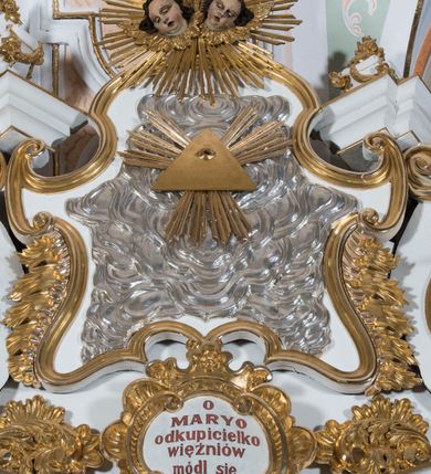 Zdjęcie nr 4: Ołtarz drewniany, prostopadłościenny. Mensa drewniana, sarkofagowa, antepedium zdobione płaskorzeźbionym kartuszem z umieszczonym w polu godłem herbu Uniwersytetu Krakowskiego na czerwonym tle.

 Nastawa architektoniczna, trójosiowa, jednokondygnacyjna ze zwieńczeniem, osadzona na dwustrefowym cokole, o osiach bocznych ustawionych ukośnie. Kondygnacja ujęta parą pilastrów oraz dwiema parami kolumn podtrzymujących przerwane belkowanie,  na którym znajduje się para puttów. W polu środkowym obraz z przedstawieniem Matki Boskiej od Odkupienia Niewolników ujęty prostokątną, profilowaną ramą zamkniętą łukiem nadwieszonym. Na cokole, po bokach obrazu ustawione dwie rzeźby: po lewej św. Kryspina, po prawej św. Kryspiniana; w osiach bocznych, w płytkich wnękach: po lewej rzeźba św. Szczepana, po prawej św. Wawrzyńca. Nad obrazem Matki Boskiej płaskorzeźbiony kartusz rocaille’owy z wpisanym w polu napisem „O / MARYO / odkupicielko / więźniów / módl się / za nami!”.

 Zwieńczenie w formie rozbudowanej aediculi, o osiach bocznych ustawionych ukośnie, z przodu flankowane dwiema wolutami z siedzącą na nich parą aniołków, zamknięte przerywanym, profilowanym gzymsem z ulokowaną na nim parą wazonów płomienistych. W polu zwieńczenia płycina wypełniona obłokami, o fantazyjnym kartuszowym wykroju z przedstawieniem Oka Opatrzności wpisanym w trójkąt na tle trzech wiązek promieni. Szczyt jest w formie promienistej glorii z parą uskrzydlonych główek anielskich.

 Kolumny złocone, ustawione na profilowanych bazach, o gładkim trzonie, kapitele w porządku kompozytowym.

 Partie cokołu zdobione prostokątnymi płycinami o wyciętych narożach.

 Struktura malowana w kolorze jasnobeżowym, ornamentyka i detale złocone i srebrzone, profilowania w kolorze czerwonym i złoconym.