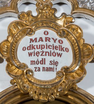 Zdjęcie nr 7: Ołtarz drewniany, prostopadłościenny. Mensa drewniana, sarkofagowa, antepedium zdobione płaskorzeźbionym kartuszem z umieszczonym w polu godłem herbu Uniwersytetu Krakowskiego na czerwonym tle.

 Nastawa architektoniczna, trójosiowa, jednokondygnacyjna ze zwieńczeniem, osadzona na dwustrefowym cokole, o osiach bocznych ustawionych ukośnie. Kondygnacja ujęta parą pilastrów oraz dwiema parami kolumn podtrzymujących przerwane belkowanie,  na którym znajduje się para puttów. W polu środkowym obraz z przedstawieniem Matki Boskiej od Odkupienia Niewolników ujęty prostokątną, profilowaną ramą zamkniętą łukiem nadwieszonym. Na cokole, po bokach obrazu ustawione dwie rzeźby: po lewej św. Kryspina, po prawej św. Kryspiniana; w osiach bocznych, w płytkich wnękach: po lewej rzeźba św. Szczepana, po prawej św. Wawrzyńca. Nad obrazem Matki Boskiej płaskorzeźbiony kartusz rocaille’owy z wpisanym w polu napisem „O / MARYO / odkupicielko / więźniów / módl się / za nami!”.

 Zwieńczenie w formie rozbudowanej aediculi, o osiach bocznych ustawionych ukośnie, z przodu flankowane dwiema wolutami z siedzącą na nich parą aniołków, zamknięte przerywanym, profilowanym gzymsem z ulokowaną na nim parą wazonów płomienistych. W polu zwieńczenia płycina wypełniona obłokami, o fantazyjnym kartuszowym wykroju z przedstawieniem Oka Opatrzności wpisanym w trójkąt na tle trzech wiązek promieni. Szczyt jest w formie promienistej glorii z parą uskrzydlonych główek anielskich.

 Kolumny złocone, ustawione na profilowanych bazach, o gładkim trzonie, kapitele w porządku kompozytowym.

 Partie cokołu zdobione prostokątnymi płycinami o wyciętych narożach.

 Struktura malowana w kolorze jasnobeżowym, ornamentyka i detale złocone i srebrzone, profilowania w kolorze czerwonym i złoconym.