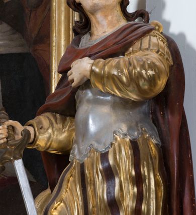 Zdjęcie nr 16: Ołtarz drewniany, prostopadłościenny. Mensa drewniana, sarkofagowa, antepedium zdobione płaskorzeźbionym kartuszem z umieszczonym w polu godłem herbu Uniwersytetu Krakowskiego na czerwonym tle.

 Nastawa architektoniczna, trójosiowa, jednokondygnacyjna ze zwieńczeniem, osadzona na dwustrefowym cokole, o osiach bocznych ustawionych ukośnie. Kondygnacja ujęta parą pilastrów oraz dwiema parami kolumn podtrzymujących przerwane belkowanie,  na którym znajduje się para puttów. W polu środkowym obraz z przedstawieniem Matki Boskiej od Odkupienia Niewolników ujęty prostokątną, profilowaną ramą zamkniętą łukiem nadwieszonym. Na cokole, po bokach obrazu ustawione dwie rzeźby: po lewej św. Kryspina, po prawej św. Kryspiniana; w osiach bocznych, w płytkich wnękach: po lewej rzeźba św. Szczepana, po prawej św. Wawrzyńca. Nad obrazem Matki Boskiej płaskorzeźbiony kartusz rocaille’owy z wpisanym w polu napisem „O / MARYO / odkupicielko / więźniów / módl się / za nami!”.

 Zwieńczenie w formie rozbudowanej aediculi, o osiach bocznych ustawionych ukośnie, z przodu flankowane dwiema wolutami z siedzącą na nich parą aniołków, zamknięte przerywanym, profilowanym gzymsem z ulokowaną na nim parą wazonów płomienistych. W polu zwieńczenia płycina wypełniona obłokami, o fantazyjnym kartuszowym wykroju z przedstawieniem Oka Opatrzności wpisanym w trójkąt na tle trzech wiązek promieni. Szczyt jest w formie promienistej glorii z parą uskrzydlonych główek anielskich.

 Kolumny złocone, ustawione na profilowanych bazach, o gładkim trzonie, kapitele w porządku kompozytowym.

 Partie cokołu zdobione prostokątnymi płycinami o wyciętych narożach.

 Struktura malowana w kolorze jasnobeżowym, ornamentyka i detale złocone i srebrzone, profilowania w kolorze czerwonym i złoconym.