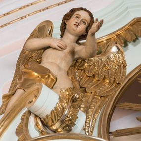 Zdjęcie nr 1: Para pełnoplastycznych, całopostaciowych figur przedstawia anioły przyklękające na przerwanym, wolutowym przyczółku zwieńczenia ołtarza. Ich zwrócone niemal w trzech czwartych, młodzieńcze sylwetki są lekko pochylone ku sobie. Owalne, szerokie twarze aniołów charakteryzują pełne, wyraziste, niemal identyczne rysy z dużymi oczami, długimi, prostymi nosami i lekko zarumienionymi policzkami. Ich falowane, brązowe, częściowo przesłaniające uszy włosy łagodnie opadają na plecy. Sylwetki aniołów, charakteryzujące się stosunkowo naturalistycznie opracowaną muskulaturą, okryte są rozwianymi, złoconymi szatami od pasa do kolan u anioła po prawej stronie i częściowo w partii bioder u anioła po lewej. Na plecach mają duże, złocone skrzydła. Anioł po lewej prawą rękę wspiera na piersiach, lewą wyciąga przed siebie, drugi obydwie składa na klatce piersiowej.      

