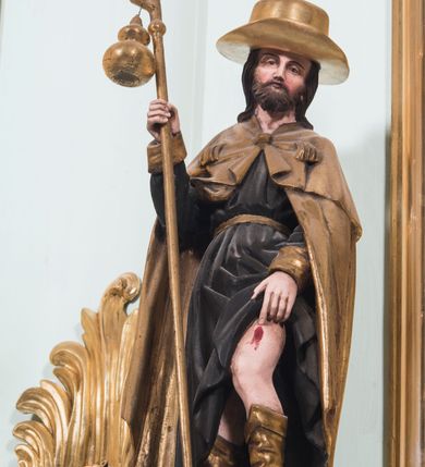 Zdjęcie nr 19: Retabulum ołtarza bocznego charakteryzuje architektoniczna, jednokondygnacyjna, jednoosiowa struktura ze zwieńczeniem. Ołtarz jest drewniany, sarkofagowy z drewnianą mensą. Retabulum osadzone jest na zdwojonym cokole. Część środkowa nastawy ujęta jest parą kolumn i dwoma parami pilastrów, z których jedna ma wklęsłe trzony. Wspomniane elementy wspierają wyłamujące się ponad nimi wklęsło-wypukłe belkowanie. Pole środkowe retabulum jest w kształcie stojącego prostokąta zamkniętego półkolistym łukiem nadwieszonym z uskokami, ujęte jest profilowaną, złoconą ramą. Zwieńczenie, w kształcie stojącego prostokąta zamknięte jest gzymsem w formie nadwieszonego łuku z uskokami. Pole środkowe stanowi owalny prześwit ujęty profilowaną, złoconą ramą. Po bokach zwieńczenia usytuowany jest przerwany, skośnie ustawiony wolutowy przyczółek. Po środku antepedium znajduje się polichromowane gorejące serce Jezusa ujęte gałązkami czerwonej róży. Pola cokołów zdobi ornamentyka rocaille’owo-akantowa. Część środkową retabulum ujmuje para ażurowych uszaków z liści akantu z motywami kogucich grzebieni. Trzony wklęsłych pilastrów w dolnej partii zdobią motywy wolut zwieńczonych liśćmi akantu. W górnej partii trzonów wszystkich pilastrów znajdują się podwieszenia w formie związanych wstążkami kompozycji kwiatowo-owocowych. Kapitele zdobione są detalami ze stylizowanych liści akantu oraz niewielkimi konsolkami z motywem palmety. Fryz dekorują motywy ornamentyki rocaille’owej. Krawędź gzymsu zwieńczenia ujęta jest rodzajem lambrekinu z pojedynczych liści o lancetowatym kształcie. W prześwit wkomponowana została promienista gloria z monogramem Jezusa pośrodku, na ciemnoczerwonym tle, ujęta wieńcem srebrzonych obłoków. W polu części środkowej retabulum znajduje się obraz Najświętsze Serce Jezusa, dodatkowo po bokach, na półkoliście wysuniętych partiach cokołu retabulum usytuowana jest para niewielkich rzeźb św. Rocha i św. Grzegorza Wielkiego. Na przerwanym przyczółku znajduje się para figur aniołów. 
Struktura retabulum utrzymana jest w pastelowym odcieniu turkusu z akcentem ciemnej czerwieni, partie detalu architektonicznego i ornamentyka są złocone i srebrzone.    
