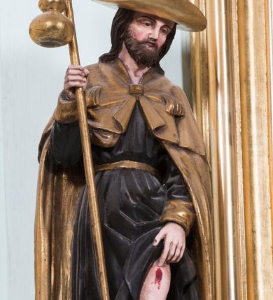 Zdjęcie nr 20: Retabulum ołtarza bocznego charakteryzuje architektoniczna, jednokondygnacyjna, jednoosiowa struktura ze zwieńczeniem. Ołtarz jest drewniany, sarkofagowy z drewnianą mensą. Retabulum osadzone jest na zdwojonym cokole. Część środkowa nastawy ujęta jest parą kolumn i dwoma parami pilastrów, z których jedna ma wklęsłe trzony. Wspomniane elementy wspierają wyłamujące się ponad nimi wklęsło-wypukłe belkowanie. Pole środkowe retabulum jest w kształcie stojącego prostokąta zamkniętego półkolistym łukiem nadwieszonym z uskokami, ujęte jest profilowaną, złoconą ramą. Zwieńczenie, w kształcie stojącego prostokąta zamknięte jest gzymsem w formie nadwieszonego łuku z uskokami. Pole środkowe stanowi owalny prześwit ujęty profilowaną, złoconą ramą. Po bokach zwieńczenia usytuowany jest przerwany, skośnie ustawiony wolutowy przyczółek. Po środku antepedium znajduje się polichromowane gorejące serce Jezusa ujęte gałązkami czerwonej róży. Pola cokołów zdobi ornamentyka rocaille’owo-akantowa. Część środkową retabulum ujmuje para ażurowych uszaków z liści akantu z motywami kogucich grzebieni. Trzony wklęsłych pilastrów w dolnej partii zdobią motywy wolut zwieńczonych liśćmi akantu. W górnej partii trzonów wszystkich pilastrów znajdują się podwieszenia w formie związanych wstążkami kompozycji kwiatowo-owocowych. Kapitele zdobione są detalami ze stylizowanych liści akantu oraz niewielkimi konsolkami z motywem palmety. Fryz dekorują motywy ornamentyki rocaille’owej. Krawędź gzymsu zwieńczenia ujęta jest rodzajem lambrekinu z pojedynczych liści o lancetowatym kształcie. W prześwit wkomponowana została promienista gloria z monogramem Jezusa pośrodku, na ciemnoczerwonym tle, ujęta wieńcem srebrzonych obłoków. W polu części środkowej retabulum znajduje się obraz Najświętsze Serce Jezusa, dodatkowo po bokach, na półkoliście wysuniętych partiach cokołu retabulum usytuowana jest para niewielkich rzeźb św. Rocha i św. Grzegorza Wielkiego. Na przerwanym przyczółku znajduje się para figur aniołów. 
Struktura retabulum utrzymana jest w pastelowym odcieniu turkusu z akcentem ciemnej czerwieni, partie detalu architektonicznego i ornamentyka są złocone i srebrzone.    
