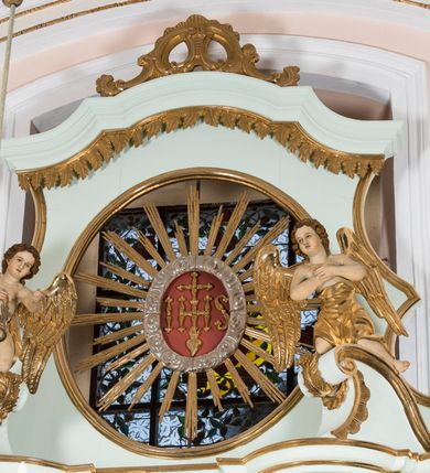Zdjęcie nr 13: Retabulum ołtarza bocznego charakteryzuje architektoniczna, jednokondygnacyjna, jednoosiowa struktura ze zwieńczeniem. Ołtarz jest drewniany, sarkofagowy z drewnianą mensą. Retabulum osadzone jest na zdwojonym cokole. Część środkowa nastawy ujęta jest parą kolumn i dwoma parami pilastrów, z których jedna ma wklęsłe trzony. Wspomniane elementy wspierają wyłamujące się ponad nimi wklęsło-wypukłe belkowanie. Pole środkowe retabulum jest w kształcie stojącego prostokąta zamkniętego półkolistym łukiem nadwieszonym z uskokami, ujęte jest profilowaną, złoconą ramą. Zwieńczenie, w kształcie stojącego prostokąta zamknięte jest gzymsem w formie nadwieszonego łuku z uskokami. Pole środkowe stanowi owalny prześwit ujęty profilowaną, złoconą ramą. Po bokach zwieńczenia usytuowany jest przerwany, skośnie ustawiony wolutowy przyczółek. Po środku antepedium znajduje się polichromowane gorejące serce Jezusa ujęte gałązkami czerwonej róży. Pola cokołów zdobi ornamentyka rocaille’owo-akantowa. Część środkową retabulum ujmuje para ażurowych uszaków z liści akantu z motywami kogucich grzebieni. Trzony wklęsłych pilastrów w dolnej partii zdobią motywy wolut zwieńczonych liśćmi akantu. W górnej partii trzonów wszystkich pilastrów znajdują się podwieszenia w formie związanych wstążkami kompozycji kwiatowo-owocowych. Kapitele zdobione są detalami ze stylizowanych liści akantu oraz niewielkimi konsolkami z motywem palmety. Fryz dekorują motywy ornamentyki rocaille’owej. Krawędź gzymsu zwieńczenia ujęta jest rodzajem lambrekinu z pojedynczych liści o lancetowatym kształcie. W prześwit wkomponowana została promienista gloria z monogramem Jezusa pośrodku, na ciemnoczerwonym tle, ujęta wieńcem srebrzonych obłoków. W polu części środkowej retabulum znajduje się obraz Najświętsze Serce Jezusa, dodatkowo po bokach, na półkoliście wysuniętych partiach cokołu retabulum usytuowana jest para niewielkich rzeźb św. Rocha i św. Grzegorza Wielkiego. Na przerwanym przyczółku znajduje się para figur aniołów. 
Struktura retabulum utrzymana jest w pastelowym odcieniu turkusu z akcentem ciemnej czerwieni, partie detalu architektonicznego i ornamentyka są złocone i srebrzone.    
