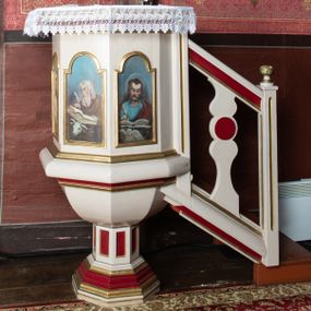 Zdjęcie nr 1: Ambona przyścienna, stojąca, z dostępem z prawej strony w postaci jednobiegowych schodów z podestem i balustradą. Kosz wsparty jest na ośmiobocznej, uskokowo profilowanej stopie, a następnie na o ośmiobocznym trzonie dekorowanym płycinami w kształcie pionowych prostokątów.

Kosz jest także na rzucie ośmioboku, z wydatną listwą cokołową u nasady, posiadającą formę masywnego wałka i profilowanym gzymsem w partii zwieńczenia. Ścianki kosza wypełnione są płycinami w kształcie pionowych prostokątów zamkniętych półkolistymi łukami nadwieszonymi, z malowanymi przedstawieniami, od lewej: św. Jana Ewangelisty, Jezusa Dobrego Pasterza, św. Łukasza Ewangelisty oraz św. Mateusza Ewangelisty. Wszystkie osoby przedstawione są w półpostaci, ewangeliści ukazani jako piszący w księgach, z atrybutami w narożach obrazów: św. Jan z orłem, św. Łukasz z wołem oraz św. Mateusz z aniołem.

 Baldachim powtarza rzut kosza ambony, o krawędzi zdobionej lambrekinem; wyżej jest zredukowane belkowanie.

 Balustrada schodów jest z jedną, sylwetowo wyciętą, dwulalkową tralką z płaskim nodusem.

 Struktura malowana jest w kolorze jasnobeżowym, detale w kolorze czerwonym, profilowania złocone.