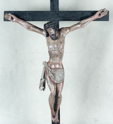 Zdjęcie nr 1: Do prostego krzyża przybita trzema gwoźdźmi pełnoplastyczna figura Chrystusa umarłego. Ciało w lekkim zwisie, o szeroko rozłożonych ramionach, głowa opadająca na prawy bark, nogi delikatnie ugięte w kolanach, stopy w układzie prawa na lewą. Chrystus ma podłużną twarz, z zamkniętymi oczami, długim, spiczastym nosem i wąskimi ustami, okoloną krótką, kręconą brodą. Włosy długie, ciemnobrązowe, silnie skręcone w pukle, opadające na plecy i prawe ramię. Na głowie szeroka korona cierniowa. Ciało szczupłe, o wyraźnie podkreślonej talii i szerokich biodrach, z delikatnie zaznaczoną muskulaturą i żebrami. Perizonium krótkie, odsłaniające prawe udo, zawiązane na prawym biodrze z opadającym wzdłuż nogi zwisem tkaniny. Polichromia ciała naturalistyczna, z zaznaczonymi śladami męki. Na zakończeniu pionowej belki krzyża kartusz z napisem „INRI”.
 
