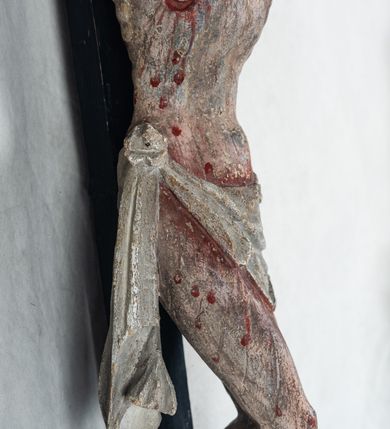 Zdjęcie nr 11: Do prostego krzyża przybita trzema gwoźdźmi pełnoplastyczna figura Chrystusa umarłego. Ciało w lekkim zwisie, o szeroko rozłożonych ramionach, głowa opadająca na prawy bark, nogi delikatnie ugięte w kolanach, stopy w układzie prawa na lewą. Chrystus ma podłużną twarz, z zamkniętymi oczami, długim, spiczastym nosem i wąskimi ustami, okoloną krótką, kręconą brodą. Włosy długie, ciemnobrązowe, silnie skręcone w pukle, opadające na plecy i prawe ramię. Na głowie szeroka korona cierniowa. Ciało szczupłe, o wyraźnie podkreślonej talii i szerokich biodrach, z delikatnie zaznaczoną muskulaturą i żebrami. Perizonium krótkie, odsłaniające prawe udo, zawiązane na prawym biodrze z opadającym wzdłuż nogi zwisem tkaniny. Polichromia ciała naturalistyczna, z zaznaczonymi śladami męki. Na zakończeniu pionowej belki krzyża kartusz z napisem „INRI”.
 
