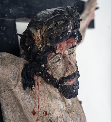 Zdjęcie nr 5: Do prostego krzyża przybita trzema gwoźdźmi pełnoplastyczna figura Chrystusa umarłego. Ciało w lekkim zwisie, o szeroko rozłożonych ramionach, głowa opadająca na prawy bark, nogi delikatnie ugięte w kolanach, stopy w układzie prawa na lewą. Chrystus ma podłużną twarz, z zamkniętymi oczami, długim, spiczastym nosem i wąskimi ustami, okoloną krótką, kręconą brodą. Włosy długie, ciemnobrązowe, silnie skręcone w pukle, opadające na plecy i prawe ramię. Na głowie szeroka korona cierniowa. Ciało szczupłe, o wyraźnie podkreślonej talii i szerokich biodrach, z delikatnie zaznaczoną muskulaturą i żebrami. Perizonium krótkie, odsłaniające prawe udo, zawiązane na prawym biodrze z opadającym wzdłuż nogi zwisem tkaniny. Polichromia ciała naturalistyczna, z zaznaczonymi śladami męki. Na zakończeniu pionowej belki krzyża kartusz z napisem „INRI”.
 
