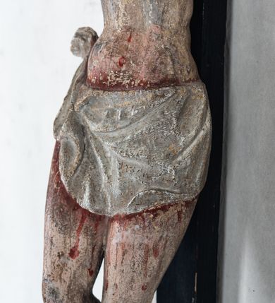 Zdjęcie nr 8: Do prostego krzyża przybita trzema gwoźdźmi pełnoplastyczna figura Chrystusa umarłego. Ciało w lekkim zwisie, o szeroko rozłożonych ramionach, głowa opadająca na prawy bark, nogi delikatnie ugięte w kolanach, stopy w układzie prawa na lewą. Chrystus ma podłużną twarz, z zamkniętymi oczami, długim, spiczastym nosem i wąskimi ustami, okoloną krótką, kręconą brodą. Włosy długie, ciemnobrązowe, silnie skręcone w pukle, opadające na plecy i prawe ramię. Na głowie szeroka korona cierniowa. Ciało szczupłe, o wyraźnie podkreślonej talii i szerokich biodrach, z delikatnie zaznaczoną muskulaturą i żebrami. Perizonium krótkie, odsłaniające prawe udo, zawiązane na prawym biodrze z opadającym wzdłuż nogi zwisem tkaniny. Polichromia ciała naturalistyczna, z zaznaczonymi śladami męki. Na zakończeniu pionowej belki krzyża kartusz z napisem „INRI”.
 
