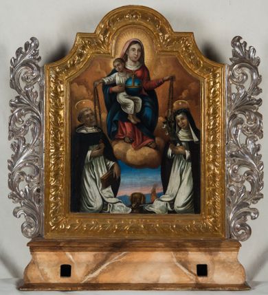 Zdjęcie nr 1: Feretron procesyjny tworzą dwa malowane na płótnie olejne obrazy ujęte w dekoracyjnie rzeźbione i złocone ramy w części górnej o fantazyjnym wykroju, ustawione na prostopadłościennym postumencie o obłych bokach. Po bokach ram znajdują się ażurowe, srebrzone uszaki utworzone ze stylizowanych wici akantowych. Na awersie feretronu umieszczono przedstawienie Matki Boskiej Różańcowej, a na rewersie św. Barbary. Ramy zdobi płaskorzeźbiony ornament roślinny z powtarzającym się motywem liścia. Postument został zaopatrzony w parę otworów do włożenia drążków umożliwiających jego noszenie. Podstawę i zwieńczenie postumentu dekoruje profilowana listwa, natomiast boki jasna brązowo-ochrowa marmoryzacja. W centrum kompozycji w obrazie z Matką Boską Różańcową ukazano siedzącą frontalnie na złocisto-ochrowych obłokach Madonnę z Dzieciątkiem. Maria ma głowę zwróconą w trzech czwartych w lewo. Prawą ręką podtrzymuje siedzącego na jej kolanach małego Jezusa, w lewej uniesionej i zgiętej w łokciu trzyma różaniec, który podaje św. Katarzynie Sieneńskiej. Madonna ma owalną twarz okoloną brązowymi włosami, wysokie czoło, wydatny, prosty nos i usta. Jej spojrzenie skierowane jest przed siebie. Ubrana jest w bladoczerwony maforion, czerwoną suknię, spod której przy szyi widać białe wykończenie koszuli oraz w błękitny płaszcz przerzucony przez prawe ramię i częściowo okrywający połą jej kolana. U dołu spod sukni widać stopy obute w sandały. Głowę Marii, podobnie jak i małego Jezusa otaczają promieniste nimby. Siedzące na jej kolanach Dzieciątko zostało ukazane w kontrapoście w trzech czwartych w lewo z głową odwróconą w prawo. Jezus lewą ręką podtrzymuje na kolanach niebieski glob ze złotym krzyżykiem, natomiast wyciągniętą prawą ręką podaje klęczącemu poniżej św. Dominikowi różaniec. Ma owalną twarz z wysokim czołem, rumiane policzki, wydatny nos i usta. Jego spojrzenie skierowane jest w stronę św. Dominika. Na głowie ma krótkie jasnobrązowe włosy odsłaniające lewe ucho. Ubrany jest w białoszarą tunikę, spod której widać bose stopy. Poniżej Madonny z lewej strony obrazu klęczy św. Dominik, a z prawej św. Katarzyna ze Sieny. Oboje zostali ujęci w trzech czwartych w białych habitach dominikańskich z czarnymi płaszczami na ramionach. Nad ich głowami widoczne są talerzowe nimby z jedną gwiazdką. Święty Dominik w lewej, nieznacznie opuszczonej ręce trzyma, przyciskając do kolona, brązową książkę. Natomiast prawą ręką odbiera od małego Jezusa różaniec dotykając złotego medalionu wiszącego na jego końcu. Jest to starszy mężczyzna z widoczną tonsurą i siwiejącym, krótkim zarostem okalającym twarz. Ma wydatny, prosty nos i usta. Swoje spojrzenie lekko uniesionej głowy kieruje w stronę Dzieciątka. Z kolei św. Katarzyna ze Sieny różaniec od Marii odbiera lewą ręką uniesioną na wysokości piersi. Także on jest zakończony złotym medalionem. W prawej dłoni święta trzyma drewniany krucyfiks i lilię. Dominikanka ma pociągłą twarz o mięsistym nosi i ustach oraz rumiane policzki. Na jej głowie widać koronę cierniową nałożoną na zakonny welon. Pomiędzy obu klęczącymi świętymi namalowano w półpostaci frontalnie ukazanego brązowego psa, trzymającego w pysku zapaloną pochodnię. W głębi widać pejzaż z motywem błękitnych wzgórz oraz wstającej jutrzenki. Na rewersie feretronu znajduje się obraz św. Barbary. Męczenniczkę przedstawiono frontalnie ujętą w trzech czwartych w prawo. Święta w uniesionej na wysokości piersi prawej ręce trzyma złoty kielich z jaśniejącą hostią charakterystycznie obróconą prawą dłonią. Hostię zdobi złoty chrystogram "IHS", trzy gwoździe u dołu oraz krzyżyk wyrastający z litery "H". Lewą ręką Barbara podtrzymuje ukośnie ułożony miecz o ciemnogranatowej rękojeści widoczny tylko do połowy. Święta ma pociągłą twarz o wysokim czole, jasną karnację, rumiane policzki, prosty nos i wydatne usta. Jej spojrzenie szeroko otwartych, ciemnych oczu skierowane jest na widza. Jej głowę otaczają długie brązowe włosy, które puklowanymi pasmami opadają na ramiona. We włosy wplecione są sznury pereł. Trzy sznury pereł dodatkowo widoczne są na wydekoltowanej szyi. Na głowie otoczonej promienistym nimbem Barbara ma złotą koronę o ostrych sterczynach zwieńczonych perłami z malowaną kameryzacją. Męczenniczka ubrana jest w taliowaną ciemnoniebieską suknię założoną na zieloną koszulę wykończoną przy rękawach i dekolcie białą koronką. Jej szyję otacza białoszara chusta spięta na piersi i na lewym ramieniu złotymi spinkami z klejnotami. Dłuższy koniec chusty udrapowany jest na prawym przedramieniu. Na ramionach namalowano osuwający się z nich czerwony płaszcz, z połą przerzuconą przez lewe przedramię. Za świętą z prawej strony widać dwupoziomową, cylindryczną wieżę nakrytą sferycznym dachem. Na górnym poziomie znajduje się okrągłe, zakratowane okno oraz fryz lombardzki biegnący pod gzymsem koronującym. Przyziemie wieży zostało przeprute odwrotnie namalowanym okienkiem strzelniczym przypominającym dziurkę od klucza.  
  