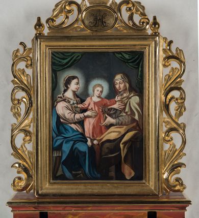 Zdjęcie nr 3: Feretron procesyjny tworzą dwa malowane na płótnie olejne obrazy w kształcie stojącego prostokąta, ujęte w profilowane i złocone ramy, ustawione na prostopadłościennym postumencie. Po bokach ram znajdują się ażurowe, złocone uszaki utworzone ze stylizowanych wici akantowych, a na górze zwieńczenie. Tworzy je złocony, dwustronny medalion z impostem, na którym umieszczono cebulastą sterczynę, flankowany ażurowym ornamentem w typie stylizowanej wici akantowej. Na końcach ramy znajdują się dwie cebulaste sterczyny, podobne do tej z impostu. W polu medalionu na awersie umieszczono monogram imienia Maria, a na rewersie chrystogram &quot;IHS&quot;. Postument został zaopatrzony w parę otworów do włożenie drążków umożliwiających noszenie feretronu. Jego podstawę i zwieńczenie  dekorują profilowane i złocone listwy, natomiast boki cynobrowo-ochrowa marmoryzacja. Na awersie feretronu znajduje się całopostaciowe przedstawienie Niepokalanego Poczęcia Najświętszej Marii Panny. Madonna została ukazana frontalnie w kontrapoście, stojąc na globie na tle szaro-brązowych, złocistych obłoków. Jej głowa otoczona promienistym nimbem jest lekko pochylona w prawo. Niepokalana prawą ręką przyciska do piersi końcówki jasnoochrowej chusty osuwającej się z jej głowy na ramiona i odsłaniającej długie brązowe włosy. Natomiast w odsuniętej od siebie lewej ręce trzyma kwiat lilii. Owalną twarz o jasnej karnacji i rumianych policzkach charakteryzują wysokie czoło, wydatny nos i usta oraz brązowe oczy ze spojrzeniem skierowanym przed siebie. Madonna ubrana jest w sięgającą stóp baldoniebieską suknię przewiązaną w talii oraz w rozwiany, niebieski płaszcz podbity purpurą, osuwający się z lewego ramienia i częściowo okrywający nogi postaci. Prawą stopą obutą w sandał Madonna depcze głowę węża z ognistym językiem, który horyzontalnie oplata niebieski glob. Natomiast pod lewą stopą widoczny jest złoty półksiężyc z rogami zwróconymi w dół. Z prawej strony Niepokalanej na wysokości jej głowy widać unoszącą się na obłoku parę uskrzydlonych główek anielskich o pucułowatych i rumianych policzkach. Na rewersie feretronu umieszczono obraz &quot;Św. Anna Samotrzeć&quot;. W centrum kompozycji na drewnianej ławie zaopatrzonej w nożycowe nogi zasiadają Maria i św. Anna, pomiędzy którymi stoi mały Jezus. Obie niewiasty zostały ukazane w całych postaciach w ujęciu trzech czwartych z twarzami zwróconymi do siebie. Maria obiema rękami podtrzymuje małego Jezusa, w czym pomaga jej św. Anna. Głowa Matki Bożej została ukazana w profilu. Otacza ją jaśniejący nimb. Madonna ma brązowe oczy, lekko zadarty nos, wydatne usta, rumiane policzki oraz długą szyję. Spod jasnobrązowej chustki widoczne są ciemnobrązowe włosy opadające na ramiona i odsłaniające prawe ucho. Madonna ubrana jest w bladoróżową suknię przewiązaną w pasie i opadający z ramion niebieski, mocno udrapowany płaszcz. Święta Anna ma owalną twarz o ostrych rysach, kanciastym nosie i wydatnych wargach. Nie ma zaznaczonego nimbu. Ubrana jest w jasnoochrowy maforion, spod którego widać rąbek białej chustki na głowie oraz fragmenty brązowej sukni spodniej. Stojący pomiędzy obiema kobietami Jezus przedstawiony został frontalnie w lekkim kontrapoście z rozłożonymi rękami i głową nieznacznie przechyloną w lewo ujętą w trzech czwartych. W prawej ręce trzyma kwietną gałązkę. Jego owalną twarz z rumianymi policzkami, o drobnym nosie, wąskich ustach i brązowych oczach otaczają krótkie jasne włosy. Wokół jego głowy widać promienisty nimb. Jezus ubrany jest w baldoczerwoną, luźną tunikę odsłaniającą bose stopy. Postacie na obrazie zostały ukazane na ciemnobrązowym tle. Ponad ich głowami widoczna jest upięta ciemnozielona kotara. 