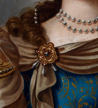 Zdjęcie nr 6: Obraz ze św. Barbarą ma kształt pionowego prostokąta zbliżonego do kwadratu. Ujmuje go drewniana rama dekorowana ornamentem roślinnym w narożach oraz geometrycznym na środku każdej z listew. Święta została przedstawiona w dwóch trzecich w ujęciu trzy czwarte w prawo na jasnobrązowym tle. Męczenniczka w charakterystycznie obróconej prawej ręce trzyma uniesiony na wysokości piersi złoty kielich z jaśniejącą hostią, zdobioną chrystogramem „IHS”. Z kolei w lewej ręce, nieznacznie wyprostowanej, ma miecz ze złotą rękojeścią. Barbara ma nieznacznie uniesioną głowę z pociągłą, owalną twarzą o jasnej karnacji z rumianymi policzkami. Charakteryzuje ją wysokie czoło, łagodna delta nosowa z prostym nosem, brązowe oczy i wąskie usta. Głowę otaczają falujące, brązowe włosy, opadające lokami na ramiona i odsłaniające fragment lewego ucha. We włosy wpleciony został sznur pereł wychodzący od owalnego, złotego, kameryzowanego klejnotu widocznego nad czołem poniżej korony. Złota korona posiada kameryzowaną obręcz oraz dziewięć ostro zakończonych sterczyn zwieńczonych perłą. Na szyi świętej znajduje się podwójny sznur pereł. Podłużna perła oprawiana w złoto widoczna jest także w jej uchu. Głowę otacza świetlisto-promienisty nimb. Święta Barbara ubrana jest w błękitną, mocno taliowaną suknię z dekoltem, odsłaniającą koronkowe, białe rękawy spodniej koszuli. Suknię dekoruje delikatny, złoty ornament roślinny. Męczenniczka ma na ramionach narzucony purpurowy płaszcz podbity zielenią, lamowany złotą taśmą. Wokół jej szyi widoczna jest jasnobrązowa chusta narzucona na płaszcz, spięta na piersiach i lewym ramieniu złotymi, owalnymi klejnotami. Klejnot na piersi dodatkowo zdobiony jest wiszącymi trzema podłużnymi perłami. Za św. Barbarą z lewej strony widoczna jest jasnobrązowa, dwupoziomowa, cylindryczna wieża z wyraźnie zaznaczonym wątkiem muru oraz fryzem koronującym, nakryta czerwonym dachem. Budowla posiada dwa nierównomiernie rozmieszczone owalne okna z kratą.  