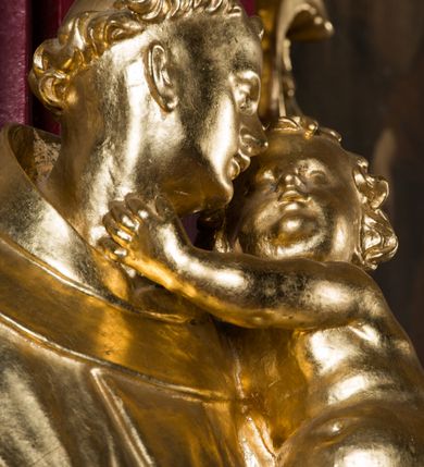 Zdjęcie nr 8: Rzeźba drążona, ustawiona na niskiej podstawie. Święty ukazany frontalnie, z głową skierowaną w lewo, w kontrapoście. Na lewym ramieniu podtrzymuje obejmujące go Dzieciątko Jezus, prawą opuszczoną wyciąga w bok. Twarz ma szczupłą, kwadratową, o podkreślonej linii żuchwy, migdałowatych, blisko siebie osadzonych oczach, małym nosie i rozchylonych ustach. Włosy ma krótkie, kręcone, na głowie tonsura. Święty ubrany jest w habit z kapturem, przepasany podwójnym szczurem ze zwisem z jednym guzem. Dzieciątko zwrócone w trzech czwartych w prawo, rączkami obejmuje głowę świętego, przepasane jest w partii podbrzusza pieluszką. Figury niemal w całości złocone, detale srebrzone.