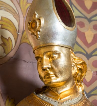 Zdjęcie nr 17: Rzeźba drążona, ustawiona na niskiej podstawie. Święty zwrócony w trzech czwartych w prawo, w kontrapoście, z pochyloną głową i lekko esowato wygiętą sylwetką. Obie ręce  ma rozłożone na boki, w lewej trzyma pastorał, prawą dłoń unosi w geście błogosławieństwa. Twarz ma szczupłą, kwadratową, o wyraźnie zarysowanej żuchwie, migdałowatych oczach, dużym nosie i wąskich, rozchylonych ustach; okoloną falowanymi włosami opadającymi na plecy. Na głowie ma infułę z taśmami (fannones). Święty ubrany jest w albę, rokietę dekorowaną płaskorzeźbioną koronką przy brzegu, stułę oraz kapę zapiętą klamrą na piersi, na dłoniach ma rękawiczki. Przy lewej nodze Stanisława popiersie mężczyzny ujęte tkaniną z głową skierowaną w górę. Figura niemal w całości złocona, detale stroju srebrzone.