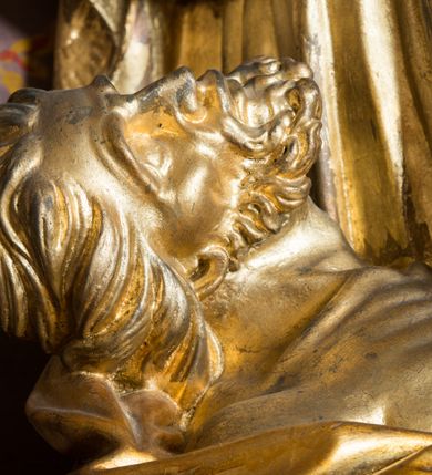 Zdjęcie nr 5: Rzeźba drążona, ustawiona na niskiej podstawie. Święty zwrócony w trzech czwartych w prawo, w kontrapoście, z pochyloną głową i lekko esowato wygiętą sylwetką. Obie ręce  ma rozłożone na boki, w lewej trzyma pastorał, prawą dłoń unosi w geście błogosławieństwa. Twarz ma szczupłą, kwadratową, o wyraźnie zarysowanej żuchwie, migdałowatych oczach, dużym nosie i wąskich, rozchylonych ustach; okoloną falowanymi włosami opadającymi na plecy. Na głowie ma infułę z taśmami (fannones). Święty ubrany jest w albę, rokietę dekorowaną płaskorzeźbioną koronką przy brzegu, stułę oraz kapę zapiętą klamrą na piersi, na dłoniach ma rękawiczki. Przy lewej nodze Stanisława popiersie mężczyzny ujęte tkaniną z głową skierowaną w górę. Figura niemal w całości złocona, detale stroju srebrzone.