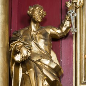 Zdjęcie nr 1: Rzeźba ścięta z tyłu i drążona, ustawiona na niskiej podstawie. Święty zwrócony frontalnie, z uniesioną głową skierowaną w lewo, w kontrapoście. Prawą ręką przytrzymuje na biodrze księgę, lewą unosi do góry w geście wskazującym dłoni, na której ma zawieszona dwa klucze. Twarz ma szczupłą, pociągłą, z wysokim czołem, oczy okrągłe, wyłupiaste, głęboko osadzone, nos garbaty, usta pełne i rozchylone. Twarz okolona krótką, gęstą brodą, włosy skręcone w pojedyncze pukle po bokach głowy, na jej czubku łysina. Święty ubrany jest w tunikę, ściśle przylegającą do ciała, marszczoną i łamaną, przepasaną w talii oraz płaszcz przerzucony przez prawe przedramię, wywinięty na lewym boku i podwieszony na prawym. Figura w całości złocona, klucze srebrzone.