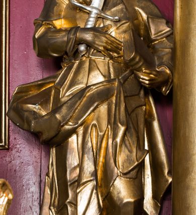 Zdjęcie nr 9: Rzeźba ścięta z tyłu i drążona, ustawiona na niskiej podstawie. 
Święty zwrócony w trzech czwartych w prawo, w kontrapoście. Lewą ręką przyciska do boku księgę, prawą kładzie na piersi i przytrzymuje miecz skierowany ostrzem w górę. Twarz ma pociągłą z wysokim czołem, o okrągłych, wyłupiastych oczach, garbatym nosie i pełnych, rozchylonych ustach; okoloną długą, rozdwajającą się brodą, opadającą na pierś oraz krótkimi, kręconymi włosami. Święty ubrany jest w tunikę ściśle przylegającą do ciała, przepasaną w talii, ostro łamaną oraz płaszcz wywinięty na prawym boku postaci, podwieszony nad lewym udem. Figura w całości złocona, miecz srebrzony. 