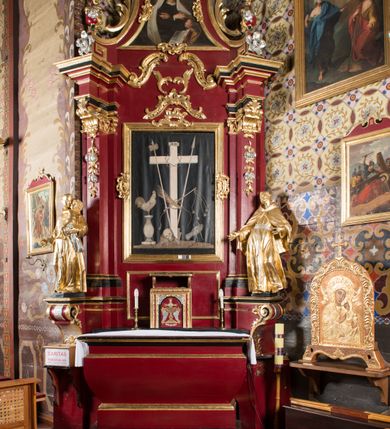 Zdjęcie nr 13: Nastawa architektoniczna, jednoosiowa, jednokondygnacyjna ze zwieńczeniem, na wysokim cokole z wyodrębnionymi konsolami. Ołtarz drewniany, sarkofagowy, na cokole, zwężający się ku dołowi z drewnianą mensą i kamiennym portatylem. Na mensie ustawione tabernakulum w formie prostopadłościennej skrzynki. Ścianka frontowa ujęta ornamentalnymi listewkami; drzwiczki w kształcie stojącego prostokąta w ornamentalnej ramie z płaskorzeźbionym przedstawieniem kielicha z hostią i winnym gronem. Nastawa ujęta parą zdwojonych pilastrów zwróconych pod kątem na zewnątrz, dekorowanych zwisami kwiatowymi, dźwigających silnie wysunięte imposty podtrzymywane przez konsole. Na tle pilastrów figury św. Antoniego Padewskiego i św. Franciszka ustawione na konsolach. W polu środkowym obraz św. Franciszka w formie stojącego prostokąta ujęty profilowaną ramą zdobioną rocaille'em. Powyżej wolutowe fragmenty rocaille'u, pod nim płycina. Zwieńczenie w formie trapezu ujętego spływami wolutowymi, dekorowanymi liśćmi palmowymi, ze ślimacznicami w kształcie meandru, spływającymi na belkowanie, na których stoją wazony. Całość zamknięta fragmentem wyłamanego trójbocznie gzymsu, zwieńczonego rokokowym szczytem z kwiatowymi gałązkami. W polu obraz św. Franciszki Rzymskiej w formie zbliżonej do zwieńczenia, ujęty ramą dekorowaną rocaille'em. Struktura polichromowana w kolorze głębokiej czerwieni, z czarnymi profilami oraz złoconymi ramami, profilami i ornamentyką.
