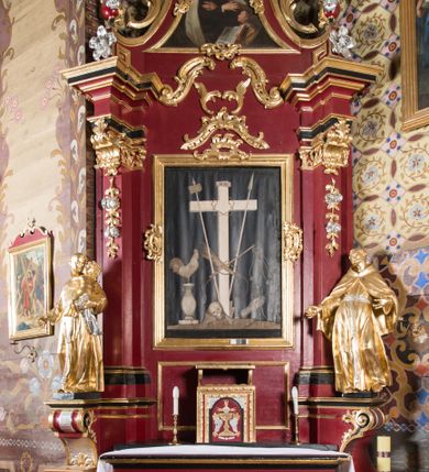 Zdjęcie nr 24: Nastawa architektoniczna, jednoosiowa, jednokondygnacyjna ze zwieńczeniem, na wysokim cokole z wyodrębnionymi konsolami. Ołtarz drewniany, sarkofagowy, na cokole, zwężający się ku dołowi z drewnianą mensą i kamiennym portatylem. Na mensie ustawione tabernakulum w formie prostopadłościennej skrzynki. Ścianka frontowa ujęta ornamentalnymi listewkami; drzwiczki w kształcie stojącego prostokąta w ornamentalnej ramie z płaskorzeźbionym przedstawieniem kielicha z hostią i winnym gronem. Nastawa ujęta parą zdwojonych pilastrów zwróconych pod kątem na zewnątrz, dekorowanych zwisami kwiatowymi, dźwigających silnie wysunięte imposty podtrzymywane przez konsole. Na tle pilastrów figury św. Antoniego Padewskiego i św. Franciszka ustawione na konsolach. W polu środkowym obraz św. Franciszka w formie stojącego prostokąta ujęty profilowaną ramą zdobioną rocaille&#039;em. Powyżej wolutowe fragmenty rocaille&#039;u, pod nim płycina. Zwieńczenie w formie trapezu ujętego spływami wolutowymi, dekorowanymi liśćmi palmowymi, ze ślimacznicami w kształcie meandru, spływającymi na belkowanie, na których stoją wazony. Całość zamknięta fragmentem wyłamanego trójbocznie gzymsu, zwieńczonego rokokowym szczytem z kwiatowymi gałązkami. W polu obraz św. Franciszki Rzymskiej w formie zbliżonej do zwieńczenia, ujęty ramą dekorowaną rocaille&#039;em. Struktura polichromowana w kolorze głębokiej czerwieni, z czarnymi profilami oraz złoconymi ramami, profilami i ornamentyką.
