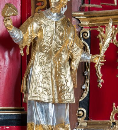 Zdjęcie nr 30: Nastawa architektoniczna, jednoosiowa, jednokondygnacyjna ze zwieńczeniem, na wysokim cokole z wyodrębnionymi konsolami. Ołtarz drewniany, sarkofagowy, na cokole, zwężający się ku dołowi z drewnianą mensą i kamiennym portatylem. Nastawa ujęta parą zdwojonych pilastrów zwróconych pod kątem na zewnątrz, dekorowanych zwisami kwiatowymi, dźwigających silnie wysunięte imposty podtrzymywane przez konsole. Na tle pilastrów figury św. Wawrzyńca i św. Szczepana ustawione na konsolach. Całe pole środkowe wypełnia wtórnie umieszczony obraz „Jezu ufam Tobie” w profilowanej ramie zdobionej rocaille&#039;em. Nad nim fragmenty rocaille&#039;u, pod nim płycina z dekoracją roślinną. Zwieńczenie w formie trapezu ujętego spływami wolutowymi, dekorowanymi liśćmi palmowymi, ze ślimacznicami w kształcie meandru, spływającymi na belkowanie, na których stoją wazony. Całość zamknięta fragmentem wyłamanego trójbocznie gzymsu, zwieńczonego rokokowym szczytem z kwiatowymi gałązkami. W polu obraz św. Wojciecha w formie zbliżonej do zwieńczenia, ujęty ramą dekorowaną rocaille&#039;em. Struktura polichromowana w kolorze głębokiej czerwieni, z czarnymi profilami oraz złoconymi ramami, profilami i ornamentyką.
