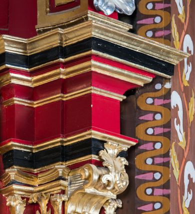 Zdjęcie nr 28: Nastawa architektoniczna, jednoosiowa, jednokondygnacyjna ze zwieńczeniem, na wysokim cokole z wyodrębnionymi konsolami. Ołtarz drewniany, sarkofagowy, na cokole, zwężający się ku dołowi z drewnianą mensą i kamiennym portatylem. Nastawa ujęta parą zdwojonych pilastrów zwróconych pod kątem na zewnątrz, dekorowanych zwisami kwiatowymi, dźwigających silnie wysunięte imposty podtrzymywane przez konsole. Na tle pilastrów figury św. Wawrzyńca i św. Szczepana ustawione na konsolach. Całe pole środkowe wypełnia wtórnie umieszczony obraz „Jezu ufam Tobie” w profilowanej ramie zdobionej rocaille'em. Nad nim fragmenty rocaille'u, pod nim płycina z dekoracją roślinną. Zwieńczenie w formie trapezu ujętego spływami wolutowymi, dekorowanymi liśćmi palmowymi, ze ślimacznicami w kształcie meandru, spływającymi na belkowanie, na których stoją wazony. Całość zamknięta fragmentem wyłamanego trójbocznie gzymsu, zwieńczonego rokokowym szczytem z kwiatowymi gałązkami. W polu obraz św. Wojciecha w formie zbliżonej do zwieńczenia, ujęty ramą dekorowaną rocaille'em. Struktura polichromowana w kolorze głębokiej czerwieni, z czarnymi profilami oraz złoconymi ramami, profilami i ornamentyką.
