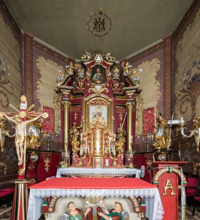 Zdjęcie nr 1: Nastawa architektoniczna, jednoosiowa, jednokondygnacyjna ze zwieńczeniem, ustawiona na dwustrefowym cokole z wyodrębnionymi prostopadłościanami. Ołtarz drewniany, prostopadłościenny z drewnianą mensą. Antepedium wydzielone ramą i wysunięte do przodu, ujęte pilastrami dźwigającymi niepełne belkowanie, w polu wieniec laurowy z rozetą, nad nim kokarda z karbowanej wstęgi flankowana przez dwa podwieszone festony z tkaniny, poniżej wić roślinna. Na ołtarzu ustawione tabernakulum w formie metalowej skrzynki w drewnianej obudowie, ujęte ustawionymi pod kątem spływami wolutowymi. Ścianka frontowa wypukła, z drewnianymi drzwiczkami w kształcie stojącego prostokąta zamkniętego łukiem półkolistym z płaskorzeźbionym kielichem z hostią i kłosami zbóż. Na nim wysoki tron wystawienia z wypukłym frontem z zamontowanym wtórnie nowym tabernakulum (wcześniej obrotowa nisza). Tron ujęty pilastrami ustawionymi pod kątem, o trzonach przechodzących w spływy wolutowe, dekorowane zwisami kwiatowymi; zwieńczony jest trzema rocaille&#039;owymi kabłąkami dekorowanymi zwisami kwiatowymi, podtrzymującymi figurkę pelikana karmiącego młode w gnieździe. Tabernakulum i tron flankowane spływami z podwieszonymi zwisami kwiatowymi zakończonymi cokołami, dźwigającymi przerwany wolutowy przyczółek z figurkami adorujących aniołów; spływy w górnej części zamknięte fragmentami gzymsu z palmetami. 
Nastawa ujęta dwiema parami pilastrów oraz stojącą na ich tle parą kolumn na cokołach dźwigających pełne belkowanie przerwane nad polem środkowym oraz fragmenty przerwanego, wolutowego przyczółka. Przed wewnętrzną parą pilastrów ustawione figury św. Piotra i św. Pawła; na belkowaniu wazony, na przyczółku putta trzymające słońce i księżyc. W polu środkowym podwójna wnęka w formie stojącego prostokąta zamkniętego łukiem odcinkowym nadwieszonym, ujęta profilowaną ramą, ze znacznie mniejszym obrazem Matki Boskiej w kształcie stojącego prostokąta. Nad nią medalion utworzony z wolut i zwisów, zwieńczony koroną otwartą. Zwieńczenie nastawy w formie trapezu ujętego wolutami spływającymi na belkowanie, zamknięte fragmentem falistego gzymsu, dekorowanym medalionem z Okiem Opatrzności w otoku z obłoków w glorii promienistej oraz gałązkami kwiatowymi. W polu obraz św. Katarzyny w formie zbliżonej do zwieńczenia, o ściętych dolnych narożach, w profilowanej ramie, z gałązkami kwiatowymi. 
Nastawa flankowana uszami utworzonymi z rocaille&#039;u, przytwierdzonymi do ściany. Ujęta parą wsporników na trumienki relikwiarzowe oraz parą dużych konsol dekorowanych rocaille&#039;m z figurami św. Mikołaja i św. Stanisława. Struktura polichromowana w kolorze głębokiej czerwieni z czarnymi profilami; kolumny, ornamentyka i profile złocone i srebrzone.