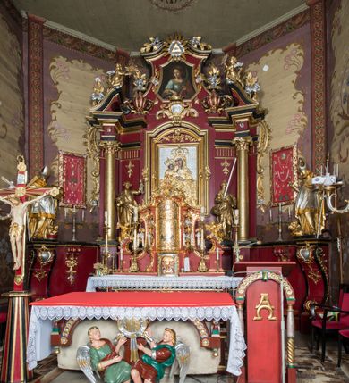 Zdjęcie nr 2: Nastawa architektoniczna, jednoosiowa, jednokondygnacyjna ze zwieńczeniem, ustawiona na dwustrefowym cokole z wyodrębnionymi prostopadłościanami. Ołtarz drewniany, prostopadłościenny z drewnianą mensą. Antepedium wydzielone ramą i wysunięte do przodu, ujęte pilastrami dźwigającymi niepełne belkowanie, w polu wieniec laurowy z rozetą, nad nim kokarda z karbowanej wstęgi flankowana przez dwa podwieszone festony z tkaniny, poniżej wić roślinna. Na ołtarzu ustawione tabernakulum w formie metalowej skrzynki w drewnianej obudowie, ujęte ustawionymi pod kątem spływami wolutowymi. Ścianka frontowa wypukła, z drewnianymi drzwiczkami w kształcie stojącego prostokąta zamkniętego łukiem półkolistym z płaskorzeźbionym kielichem z hostią i kłosami zbóż. Na nim wysoki tron wystawienia z wypukłym frontem z zamontowanym wtórnie nowym tabernakulum (wcześniej obrotowa nisza). Tron ujęty pilastrami ustawionymi pod kątem, o trzonach przechodzących w spływy wolutowe, dekorowane zwisami kwiatowymi; zwieńczony jest trzema rocaille'owymi kabłąkami dekorowanymi zwisami kwiatowymi, podtrzymującymi figurkę pelikana karmiącego młode w gnieździe. Tabernakulum i tron flankowane spływami z podwieszonymi zwisami kwiatowymi zakończonymi cokołami, dźwigającymi przerwany wolutowy przyczółek z figurkami adorujących aniołów; spływy w górnej części zamknięte fragmentami gzymsu z palmetami. 
Nastawa ujęta dwiema parami pilastrów oraz stojącą na ich tle parą kolumn na cokołach dźwigających pełne belkowanie przerwane nad polem środkowym oraz fragmenty przerwanego, wolutowego przyczółka. Przed wewnętrzną parą pilastrów ustawione figury św. Piotra i św. Pawła; na belkowaniu wazony, na przyczółku putta trzymające słońce i księżyc. W polu środkowym podwójna wnęka w formie stojącego prostokąta zamkniętego łukiem odcinkowym nadwieszonym, ujęta profilowaną ramą, ze znacznie mniejszym obrazem Matki Boskiej w kształcie stojącego prostokąta. Nad nią medalion utworzony z wolut i zwisów, zwieńczony koroną otwartą. Zwieńczenie nastawy w formie trapezu ujętego wolutami spływającymi na belkowanie, zamknięte fragmentem falistego gzymsu, dekorowanym medalionem z Okiem Opatrzności w otoku z obłoków w glorii promienistej oraz gałązkami kwiatowymi. W polu obraz św. Katarzyny w formie zbliżonej do zwieńczenia, o ściętych dolnych narożach, w profilowanej ramie, z gałązkami kwiatowymi. 
Nastawa flankowana uszami utworzonymi z rocaille'u, przytwierdzonymi do ściany. Ujęta parą wsporników na trumienki relikwiarzowe oraz parą dużych konsol dekorowanych rocaille'm z figurami św. Mikołaja i św. Stanisława. Struktura polichromowana w kolorze głębokiej czerwieni z czarnymi profilami; kolumny, ornamentyka i profile złocone i srebrzone.
