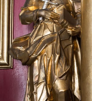 Zdjęcie nr 20: Nastawa architektoniczna, jednoosiowa, jednokondygnacyjna ze zwieńczeniem, ustawiona na dwustrefowym cokole z wyodrębnionymi prostopadłościanami. Ołtarz drewniany, prostopadłościenny z drewnianą mensą. Antepedium wydzielone ramą i wysunięte do przodu, ujęte pilastrami dźwigającymi niepełne belkowanie, w polu wieniec laurowy z rozetą, nad nim kokarda z karbowanej wstęgi flankowana przez dwa podwieszone festony z tkaniny, poniżej wić roślinna. Na ołtarzu ustawione tabernakulum w formie metalowej skrzynki w drewnianej obudowie, ujęte ustawionymi pod kątem spływami wolutowymi. Ścianka frontowa wypukła, z drewnianymi drzwiczkami w kształcie stojącego prostokąta zamkniętego łukiem półkolistym z płaskorzeźbionym kielichem z hostią i kłosami zbóż. Na nim wysoki tron wystawienia z wypukłym frontem z zamontowanym wtórnie nowym tabernakulum (wcześniej obrotowa nisza). Tron ujęty pilastrami ustawionymi pod kątem, o trzonach przechodzących w spływy wolutowe, dekorowane zwisami kwiatowymi; zwieńczony jest trzema rocaille&#039;owymi kabłąkami dekorowanymi zwisami kwiatowymi, podtrzymującymi figurkę pelikana karmiącego młode w gnieździe. Tabernakulum i tron flankowane spływami z podwieszonymi zwisami kwiatowymi zakończonymi cokołami, dźwigającymi przerwany wolutowy przyczółek z figurkami adorujących aniołów; spływy w górnej części zamknięte fragmentami gzymsu z palmetami. 
Nastawa ujęta dwiema parami pilastrów oraz stojącą na ich tle parą kolumn na cokołach dźwigających pełne belkowanie przerwane nad polem środkowym oraz fragmenty przerwanego, wolutowego przyczółka. Przed wewnętrzną parą pilastrów ustawione figury św. Piotra i św. Pawła; na belkowaniu wazony, na przyczółku putta trzymające słońce i księżyc. W polu środkowym podwójna wnęka w formie stojącego prostokąta zamkniętego łukiem odcinkowym nadwieszonym, ujęta profilowaną ramą, ze znacznie mniejszym obrazem Matki Boskiej w kształcie stojącego prostokąta. Nad nią medalion utworzony z wolut i zwisów, zwieńczony koroną otwartą. Zwieńczenie nastawy w formie trapezu ujętego wolutami spływającymi na belkowanie, zamknięte fragmentem falistego gzymsu, dekorowanym medalionem z Okiem Opatrzności w otoku z obłoków w glorii promienistej oraz gałązkami kwiatowymi. W polu obraz św. Katarzyny w formie zbliżonej do zwieńczenia, o ściętych dolnych narożach, w profilowanej ramie, z gałązkami kwiatowymi. 
Nastawa flankowana uszami utworzonymi z rocaille&#039;u, przytwierdzonymi do ściany. Ujęta parą wsporników na trumienki relikwiarzowe oraz parą dużych konsol dekorowanych rocaille&#039;m z figurami św. Mikołaja i św. Stanisława. Struktura polichromowana w kolorze głębokiej czerwieni z czarnymi profilami; kolumny, ornamentyka i profile złocone i srebrzone.